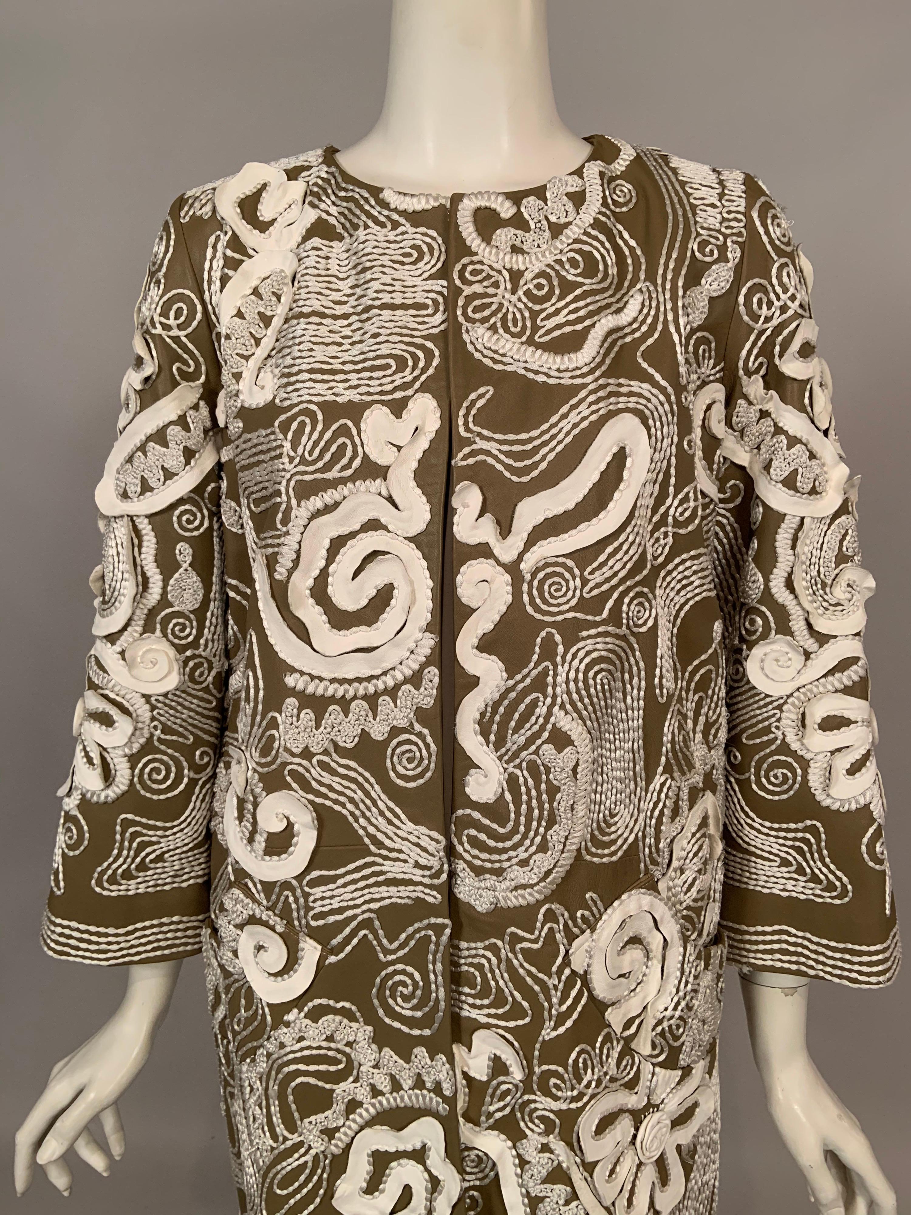 Undulating strips of white leather combined with fanciful hand embroidered white silk threads create a striking and whimsical surface design for this khaki colored lambskin leather coat designed by Oscar de la Renta. The design of the coat is spare