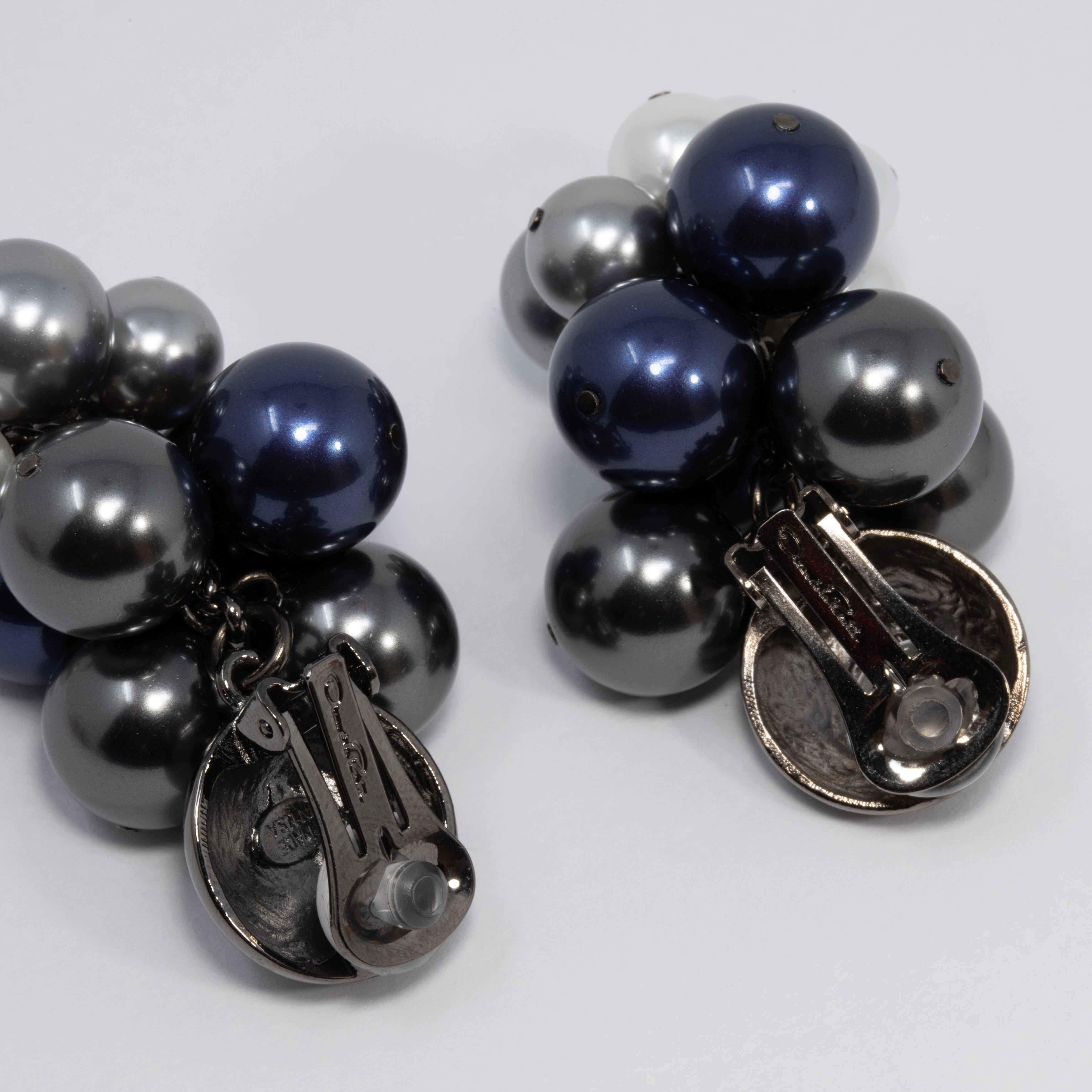 A pair of Oscar de la Renta clip on earrings. Each features a cluster or blue, gray, and white-toned faux pearls of various sizes. Bold and stylish! 

Hallmarks: Oscar de la Renta, Made in USA