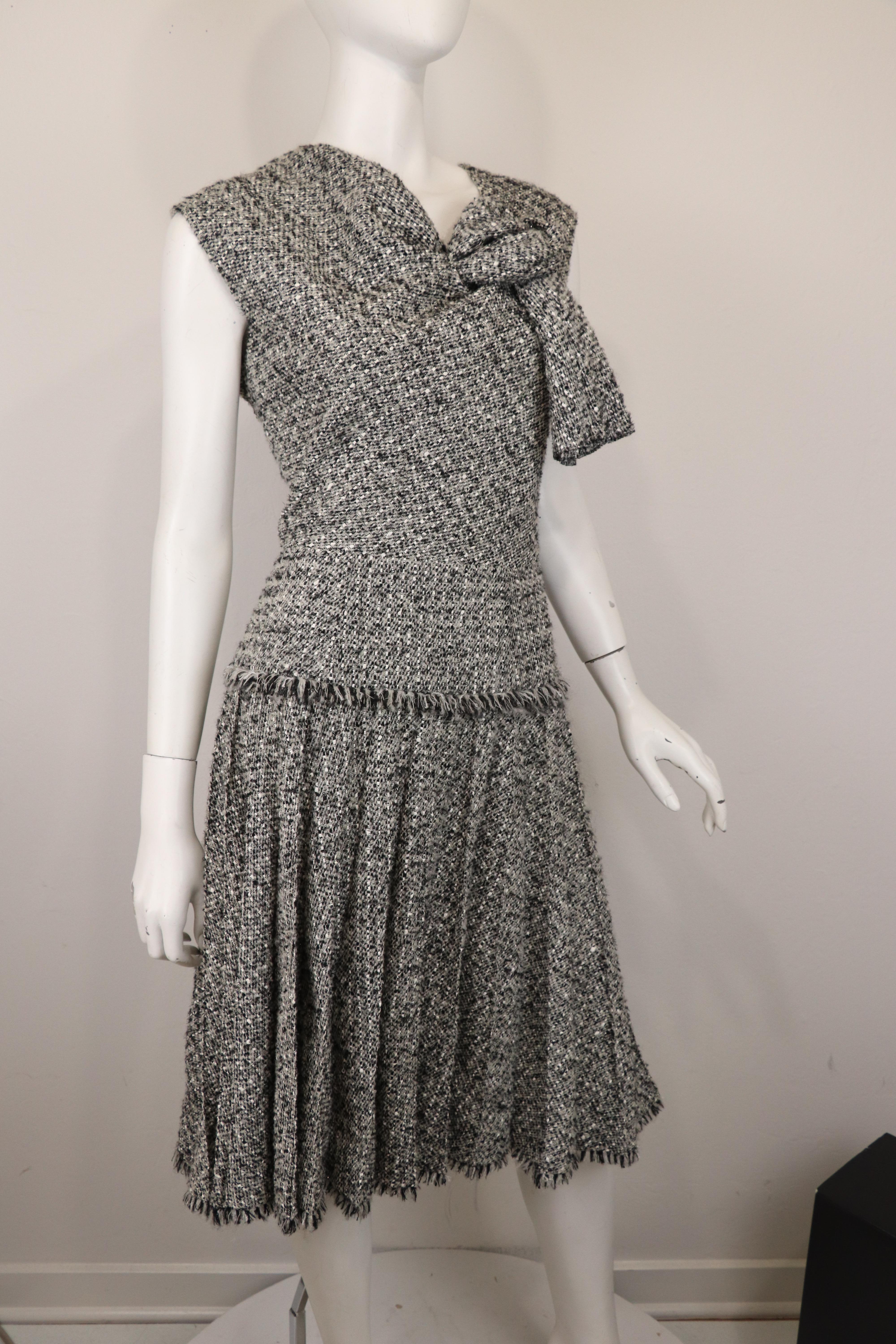 This beautiful sleeveless fit and flare Oscar de la Renta dress offers a stunning silhouette with its metallic woven fabric composed of grey, black and cream and a knotted neckline with a defined waist and a pleated skirt. Dress is fully lined in