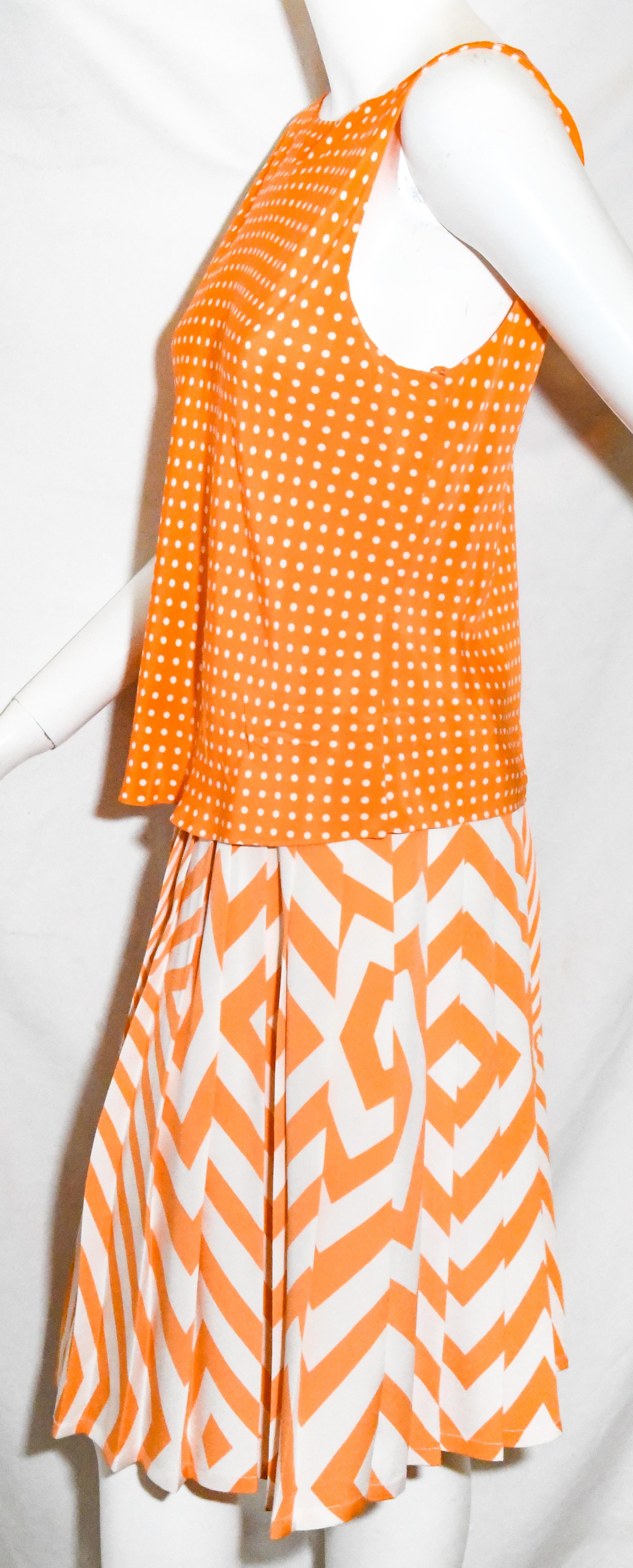 Oscar de la Renta orange and white two piece dress that incorporates a polka dot sleeveless top and an abstract  geometric pleated skirt.  The top contains 5 snaps, at back, for closure.  The pleated skirt includes a hook and eye and zipper, for