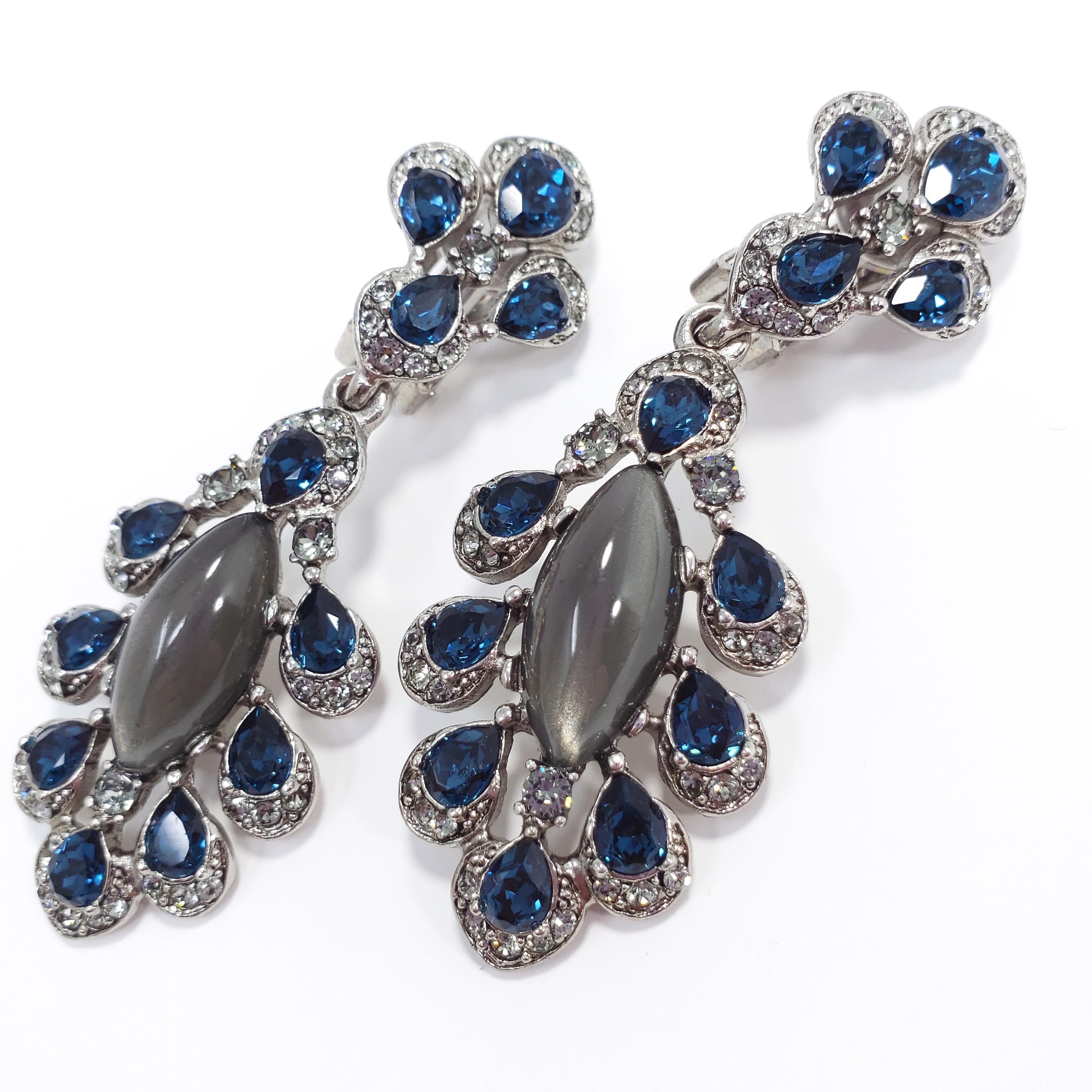 A pair of Oscar de la Renta dangling clip on earrings from the parlor collection. Feature dark blue and gray/clear crystals with centerpiece gray moonglow cabochons. Silvertone setting.

Hallmarks: Oscar de la Renta, Made in USA