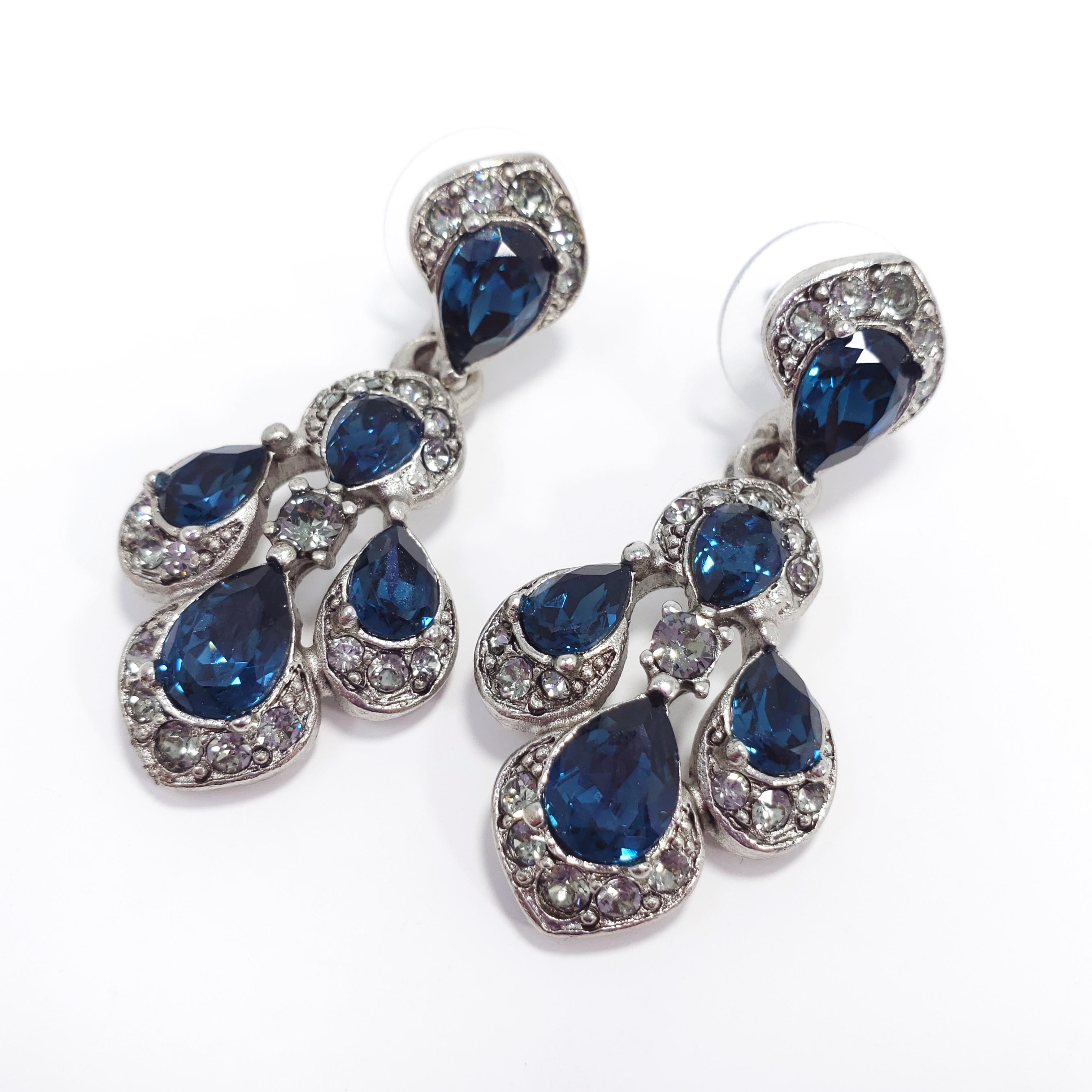 A pair of Oscar de la Renta dangling clip on earrings from the parlor collection. Feature dark blue and gray/clear crystals with centerpiece gray moonglow cabochons. Silvertone setting.

Hallmarks: Oscar de la Renta, Made in USA