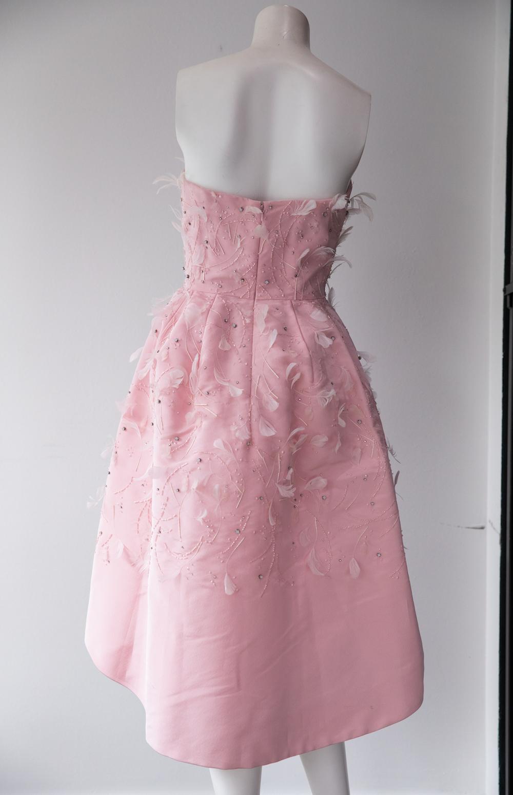 Robe à jupe intégrale rose layette d'Oscar De La Renta. Cette robe de soirée sans bretelles et à jupe ample arrive au genou. Il rappelle le glamour des années 1950 avec ses plumes roses coordonnées et ses perles sur l'ensemble du corps, et il est