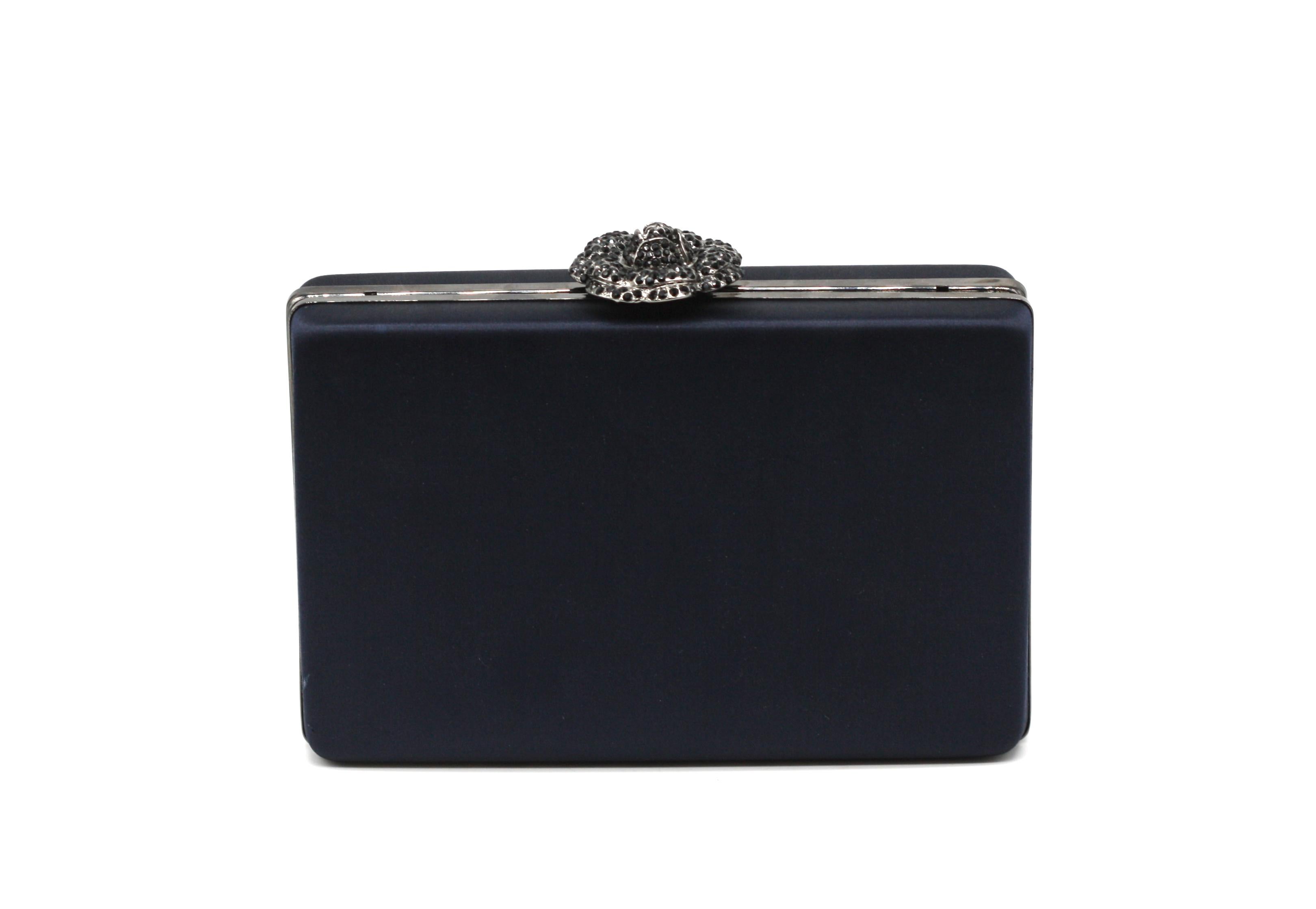 
Oscar De La Renta, Un bolso de noche cubierto de satén
De forma rectangular, la caja rígida estructurada de satén negro está coronada con un cierre floral de metal negro engastado. El interior está forrado de cuero rojo y lleva una delicada correa