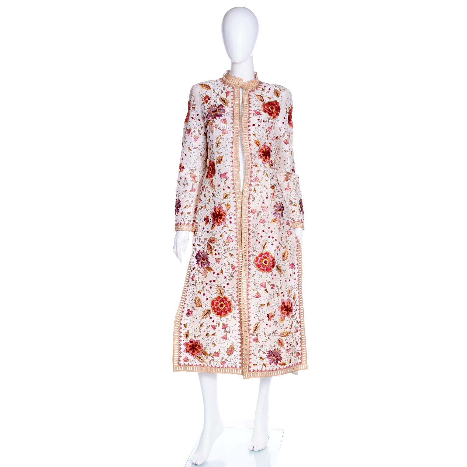 This is an absolutely stunning long vintage jacket by Oscar de la Renta. It luxurious white silk with heavily embroidered botanical and floral designs. This summer coat has a standing collar with gold embroidery and cutwork rectangles down the front