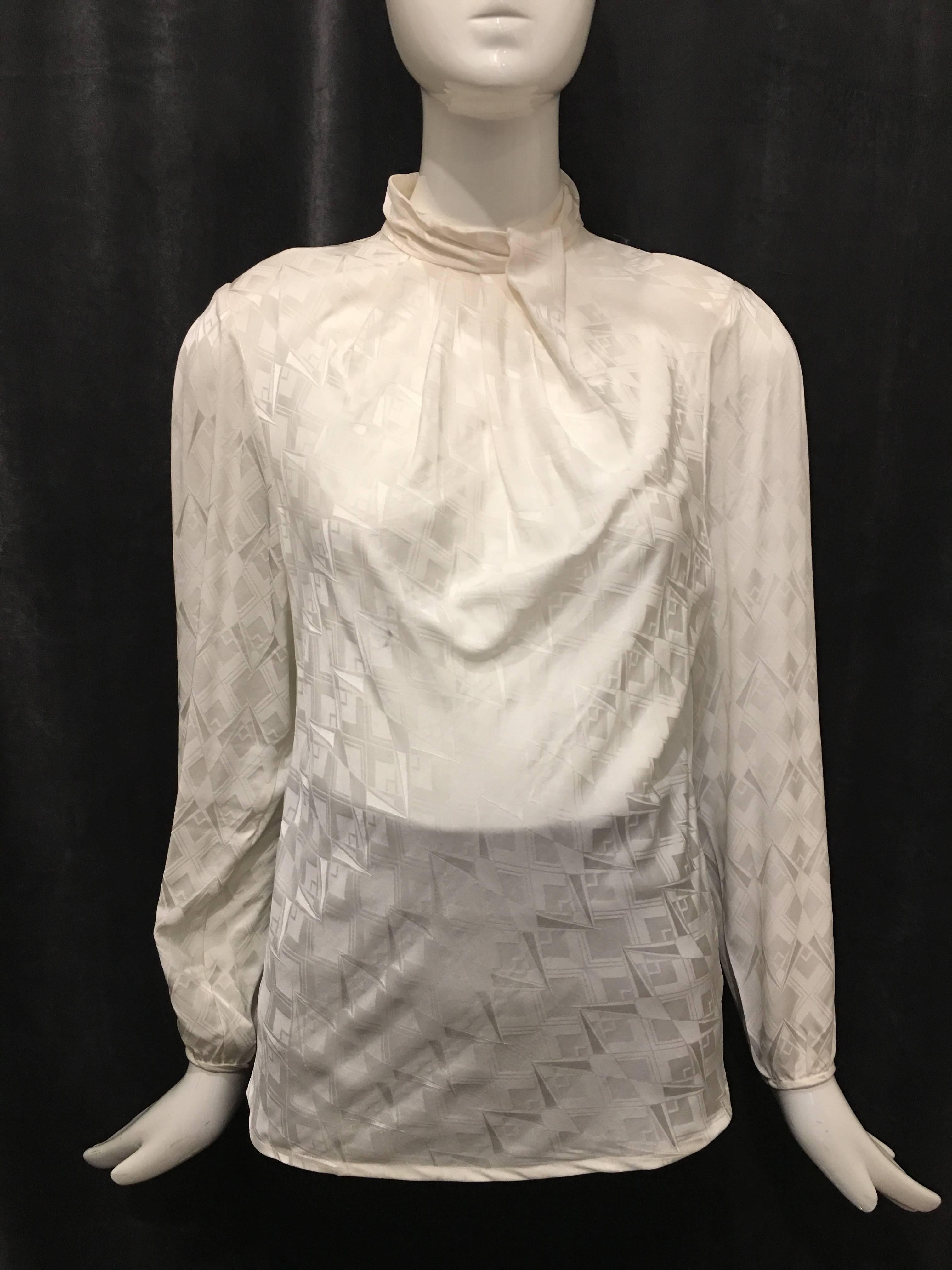 White silk blouse with all-over abstract design. Single buttons at wrists of each sleeve. Wrists are slightly gathered. Three buttons at back neckline with keyhole below. Seam down back of blouse. Slight pleating at front neckline. Slight shoulder