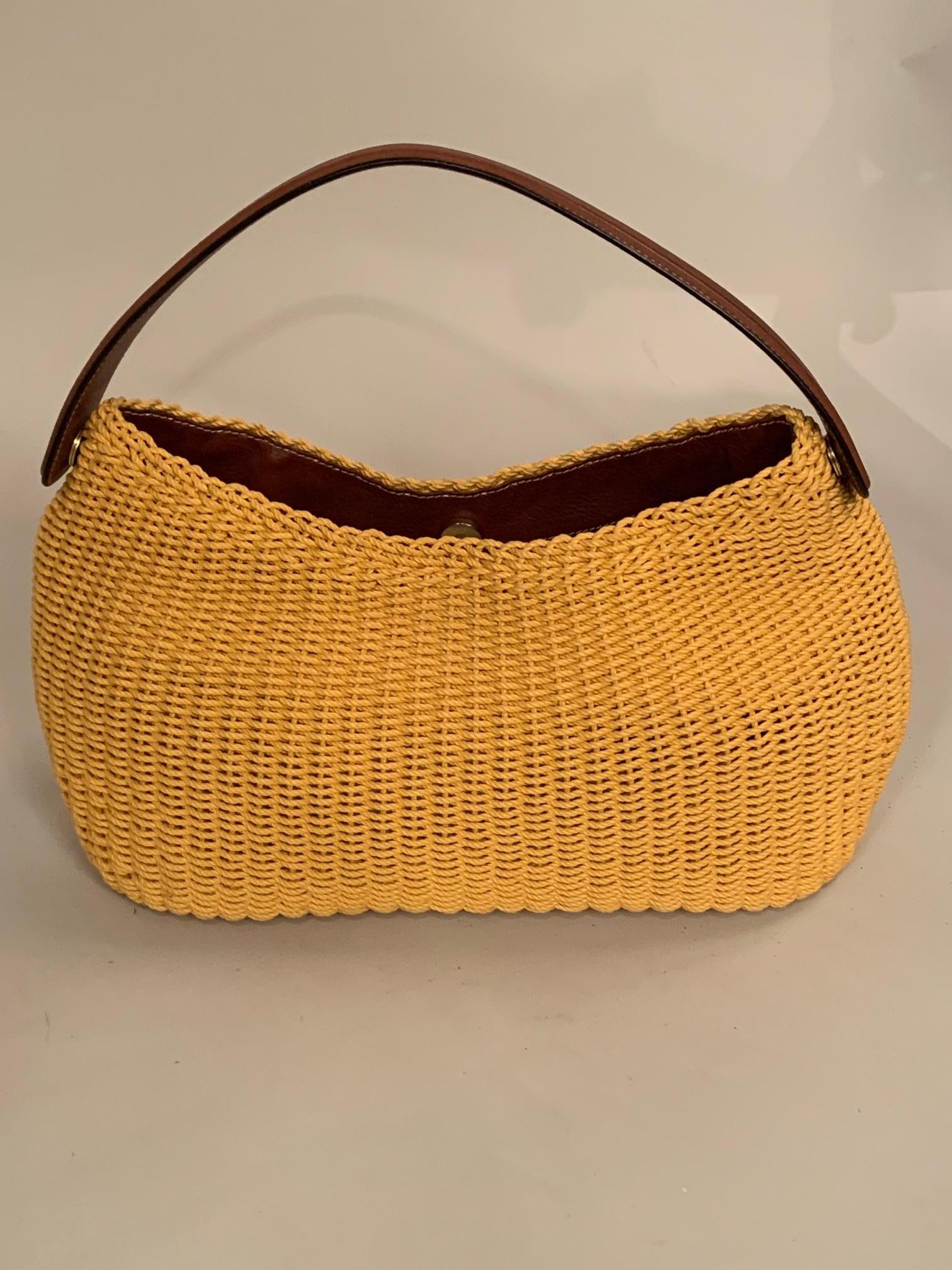 A cheery yellow woven bag from Oscar de la Renta has a chic flat leather strap handle. The bag has a snap closure and the interior is trimmed with more matching leather. The lining is a plaid fabric in orange, brown and gold. There is a zippered