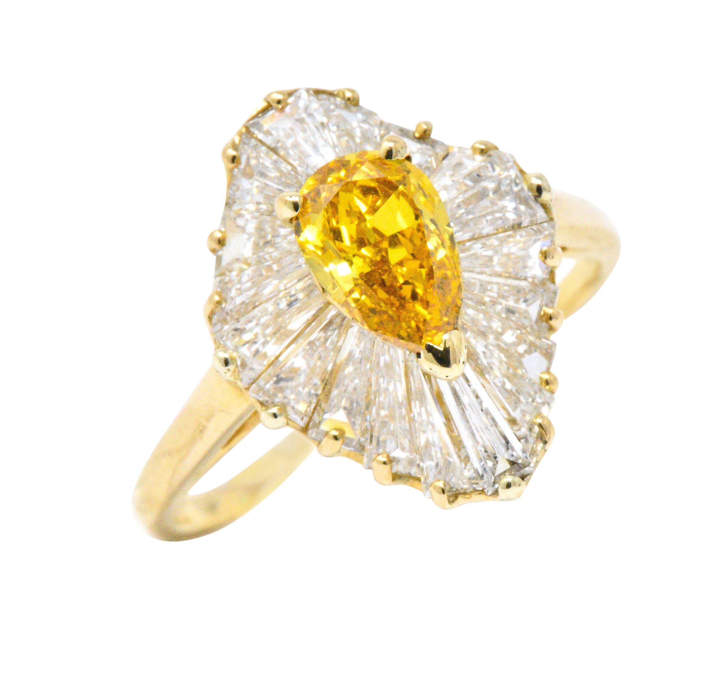 Centering a pear cut fancy colored diamond weighing 0.74 carat, natural vivid yellow-orange in color with VS2  clarity

Surrounded by a dynamic ballerina halo of tapered baguette cut diamonds weighing 
approximately 2.00 carats, E/F color with VS