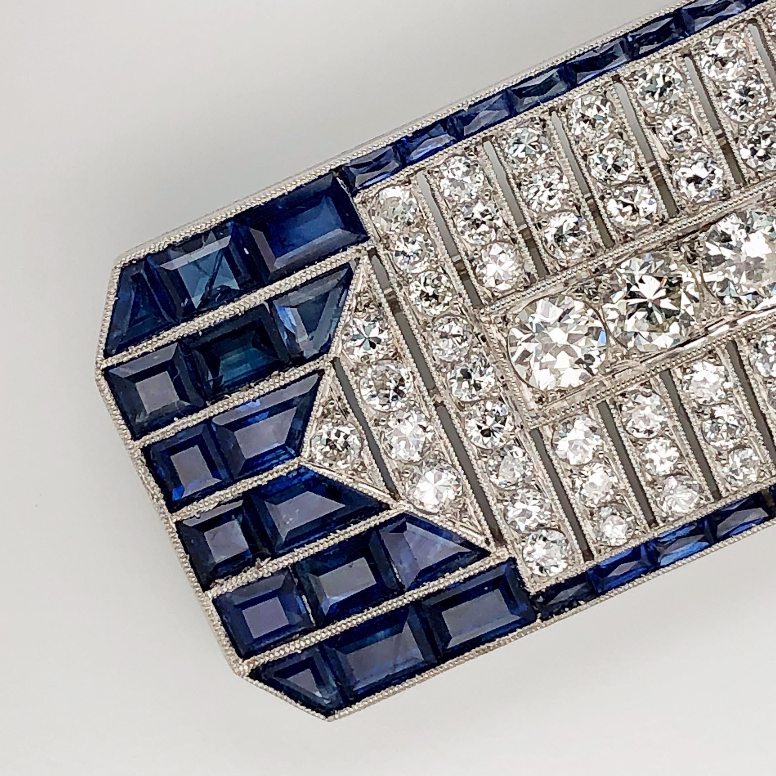 This estate Oscar Heyman platinum brooch contains 121 old European cut diamonds (~9cts) and 74 baguette and square sapphires (~16cts). Center diamond measures 6mm; quality is not indicated. 

The dimensions are 2'' L x 0.75'' W. Trombone clasp runs