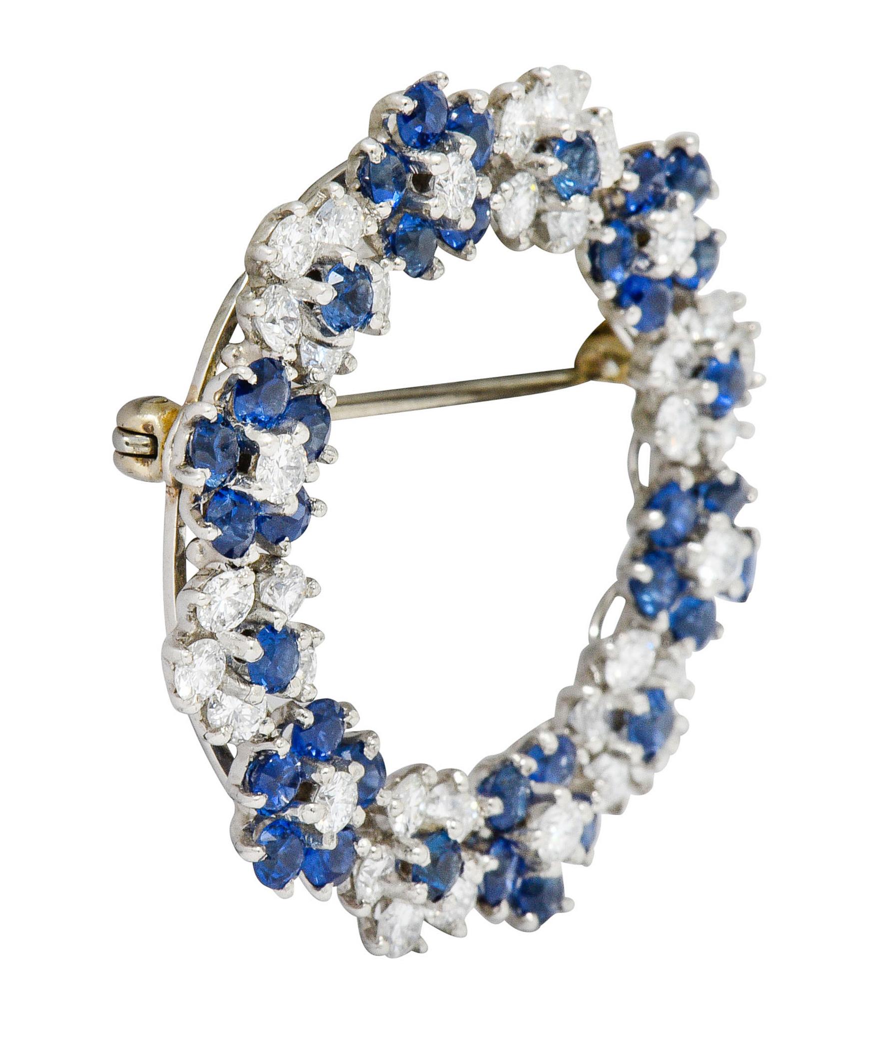 Circular brooch is designed with floral clusters of sapphire and diamonds

Round brilliant cut diamonds weigh in total approximately 2.16 carats; F/G color with VS clarity

Round cut sapphires are bright blue in color, well-matched, and weigh