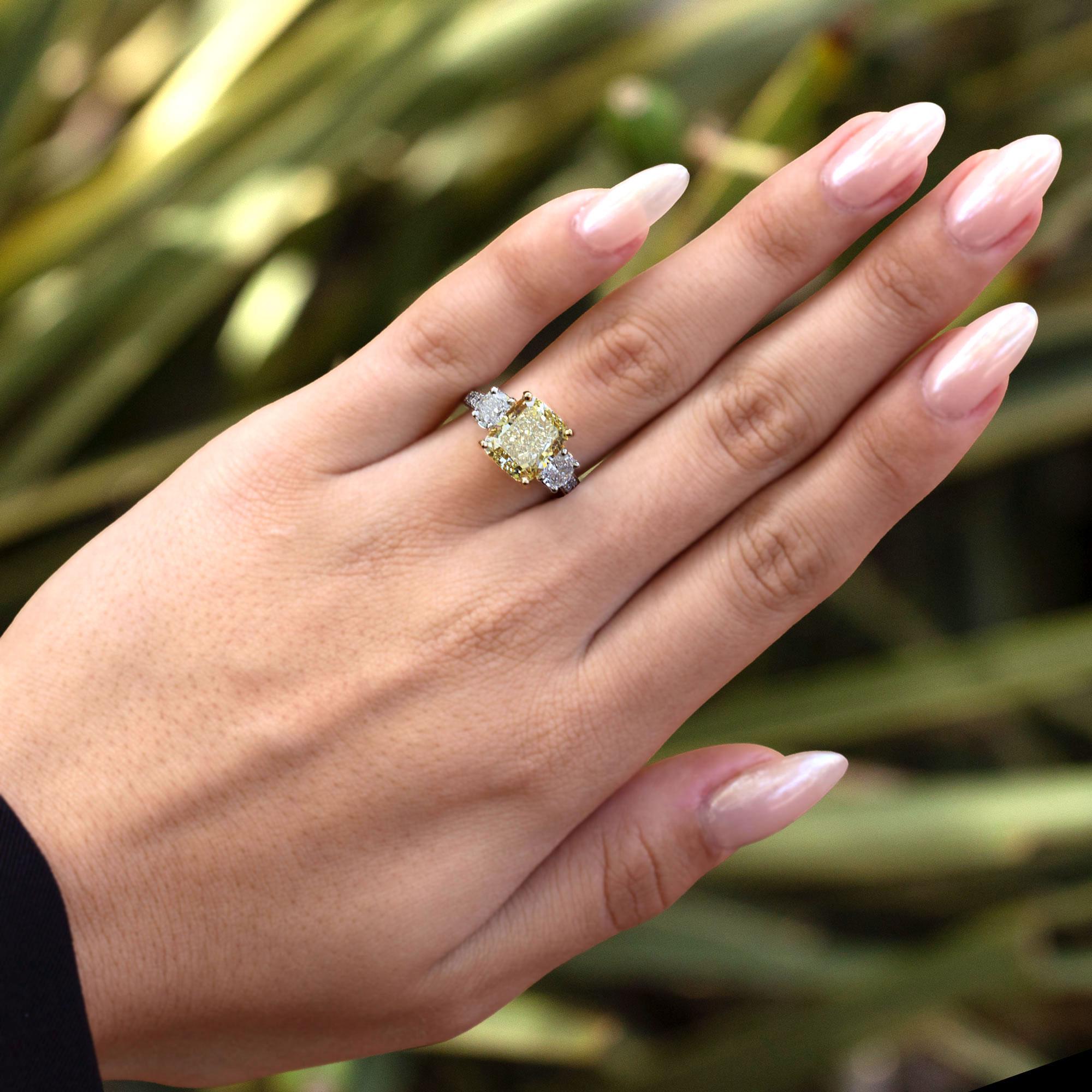 A rare opportunity to own a fabulous GIA certified fancy yellow diamond 3 stone engagement ring from legacy jewelers Oscar Heyman. Centered by a dazzling 5.04 carat cushion cut diamond flashing a vibrant, sun-kissed yellow with sparkling VS clarity.