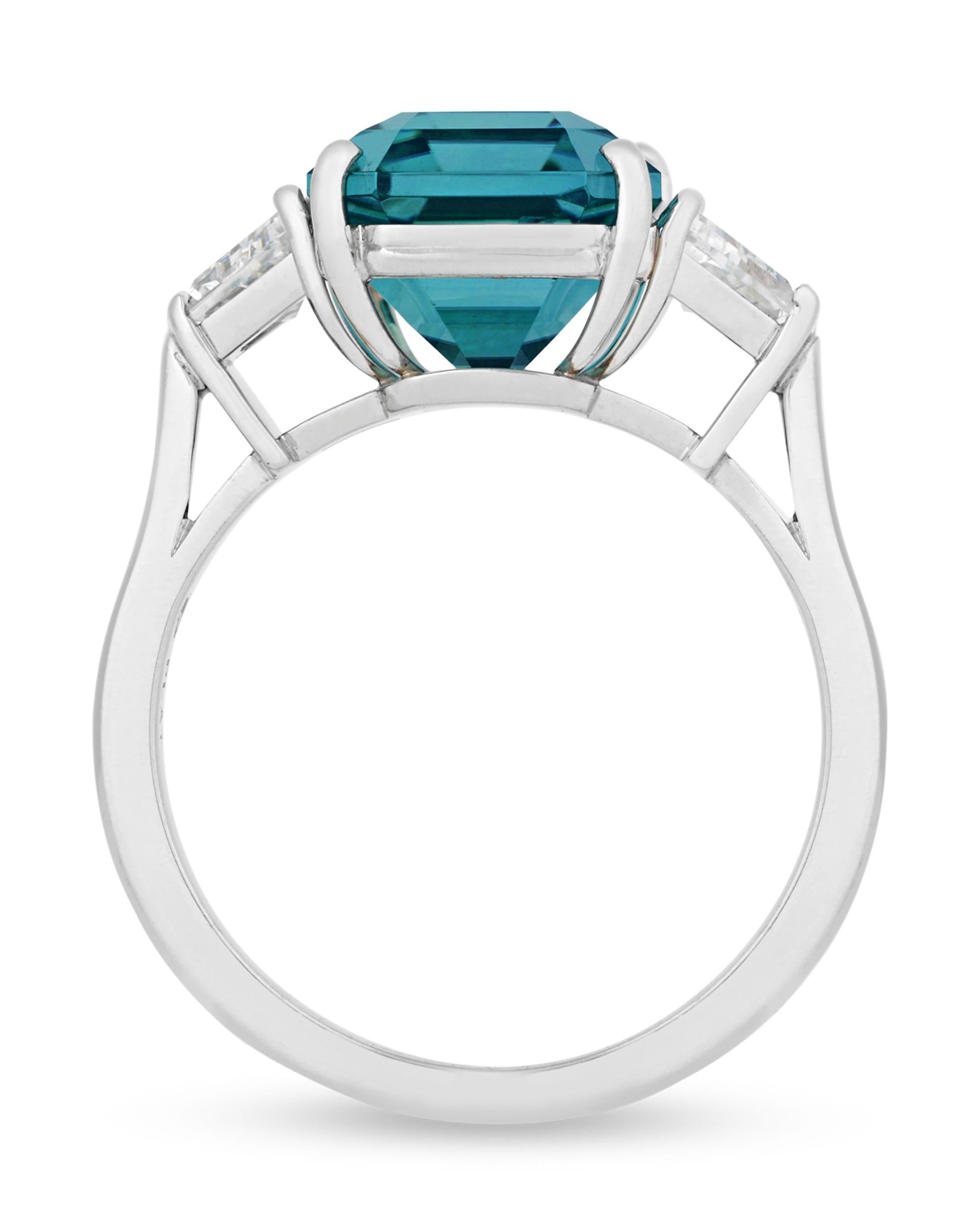 The emerald-cut lagoon tourmaline centering this elegant ring from American jeweler Oscar Heyman showcases a remarkable greenish-blue hue. Weighing 5.45 carats, the gemstone is certified by C. Dunaigre as bearing an excellent quality grade. Flanked