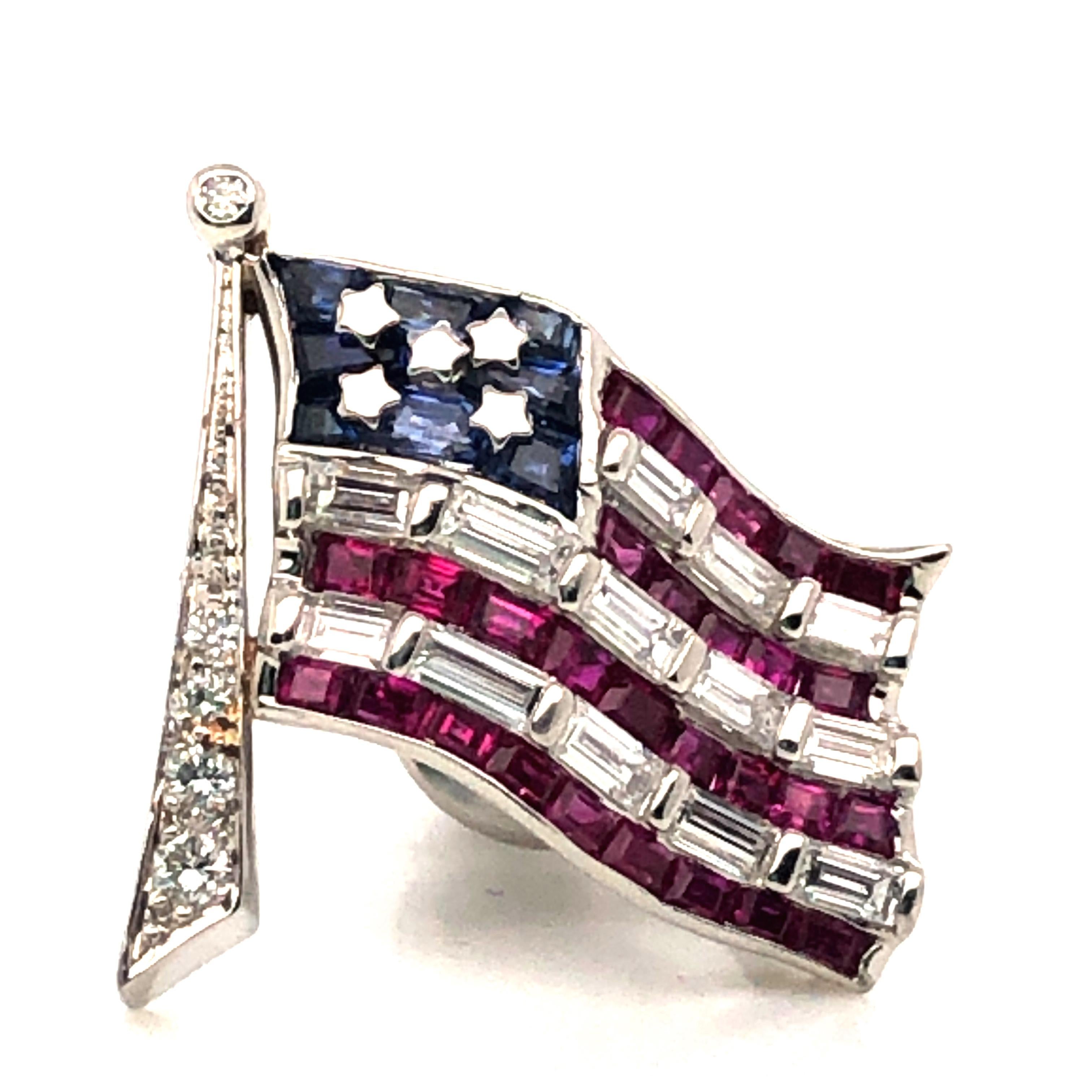 Le pin's American Flag en platine d'Oscar Heyman contient des rubis (4,87cts), des saphirs (2,40cts) et des diamants (0,52cts). Il porte la marque du fabricant, IRID PLAT, et un numéro de série unique. Il fait partie de la Collection Americana, qui