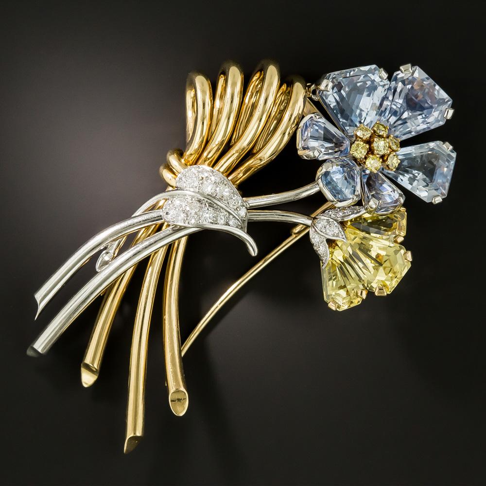 Measuring a striking 3 and 1/8 inches, this chic and stunning mid-20th-century jewel by Oscar Heyman glistens and glows with a pair of bright and beautiful flowers, with petals composed of bright blue step-cut calf's-head sapphires (natural