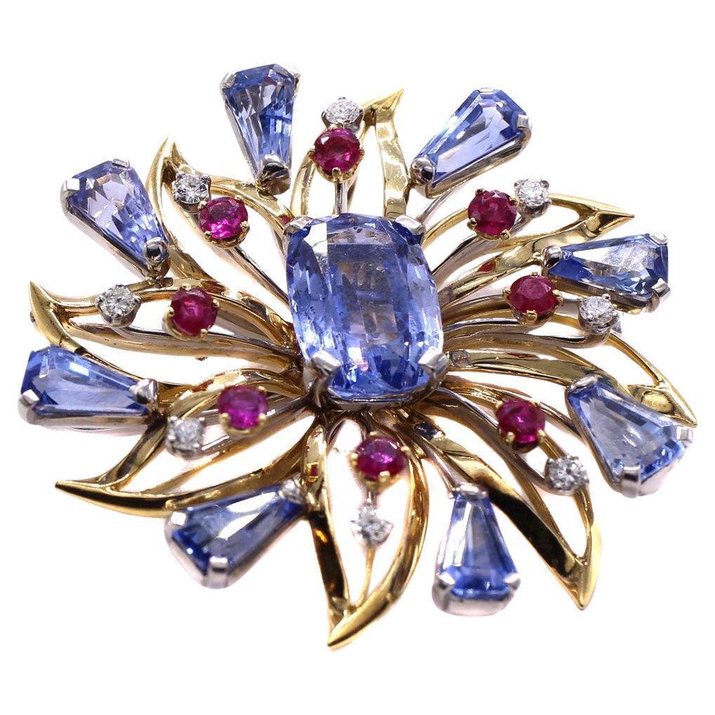 Beautifully designed and masterfully handcrafted by the renown American jeweler Oscar Heyman, this 18 karat Retro brooch is a stunning piece of vintage jewelry from the 1950s. Set with perfectly matched pastel blue natural sapphires, vibrant red