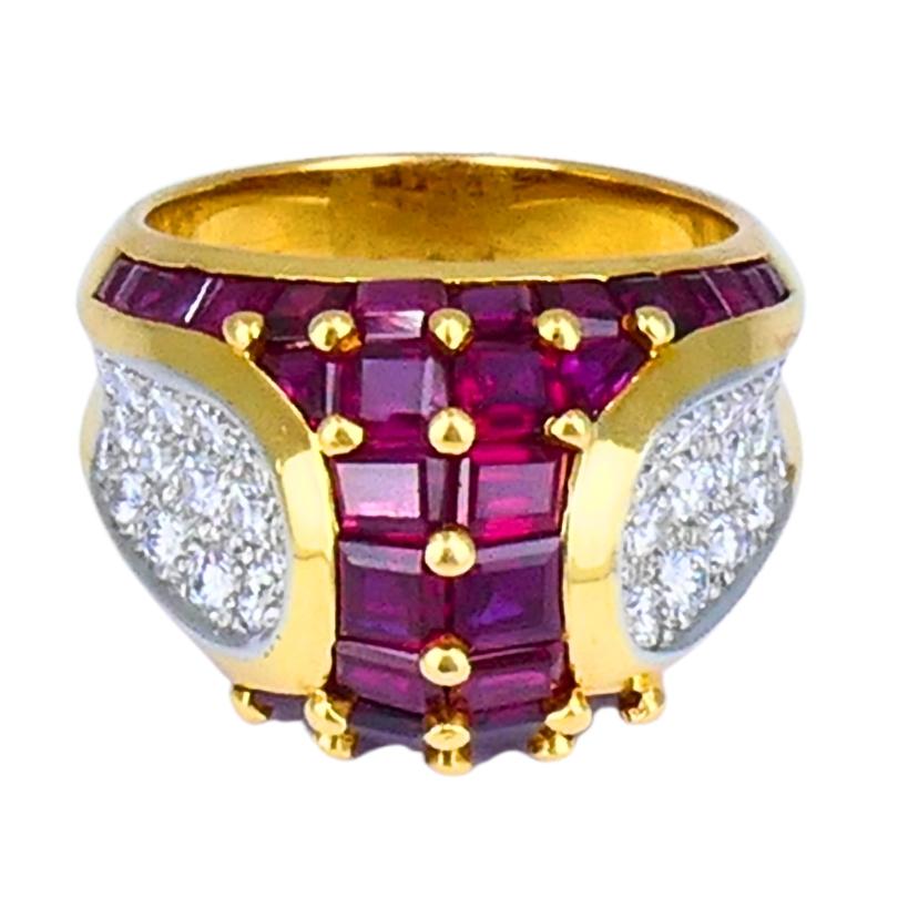 A stunning Oscar Heyman vintage cocktail ring, crafted in 18k gold and platinum, featuring a bold arrangement of rubies and diamonds.
The center showcases three rows of rectangular, channel-set rubies in a deep red hue. These are framed on each side