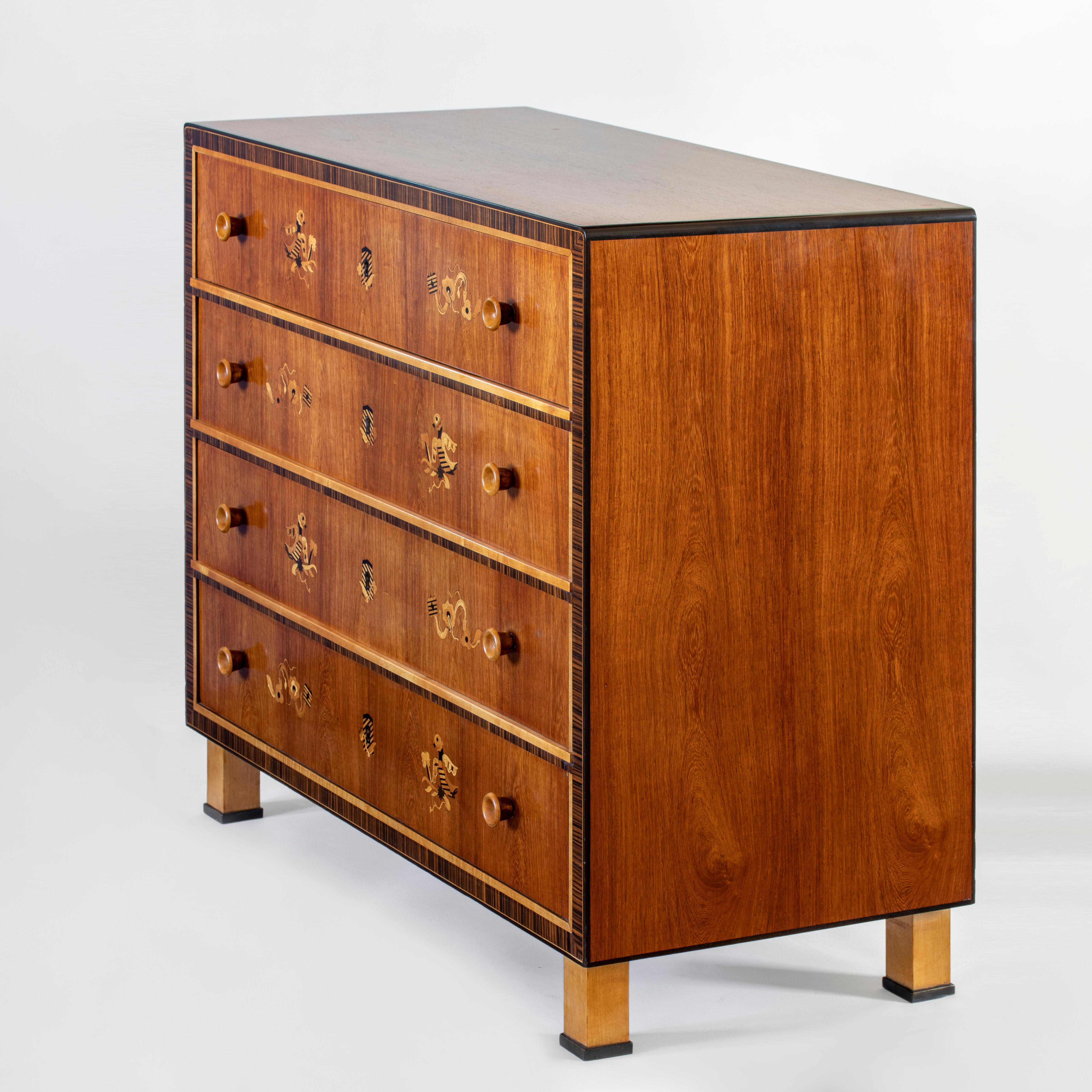 A unique commode exquisitely crafted of the finest of materials. The reverse-bookmatched cocobolo top, above four stacked drawers within a Macassar ebony and pearwood frame, each drawer displaying stylized birds and sprigs of foliate in marquetry