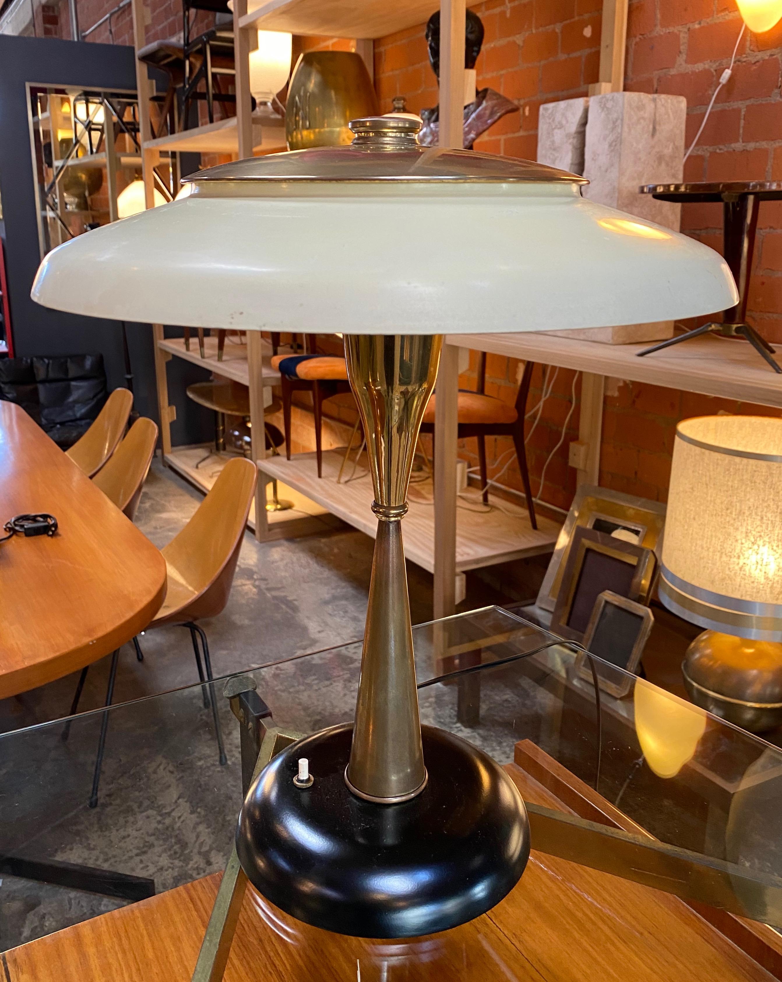 This wonderful brass desk light features a brass body and a white coated shade. The circular base of the lamp is finished in black lacquered metal. Perfect balance of the top and the bottom. Sculptural table lamp designed by Oscar Torlasco for LUMI,