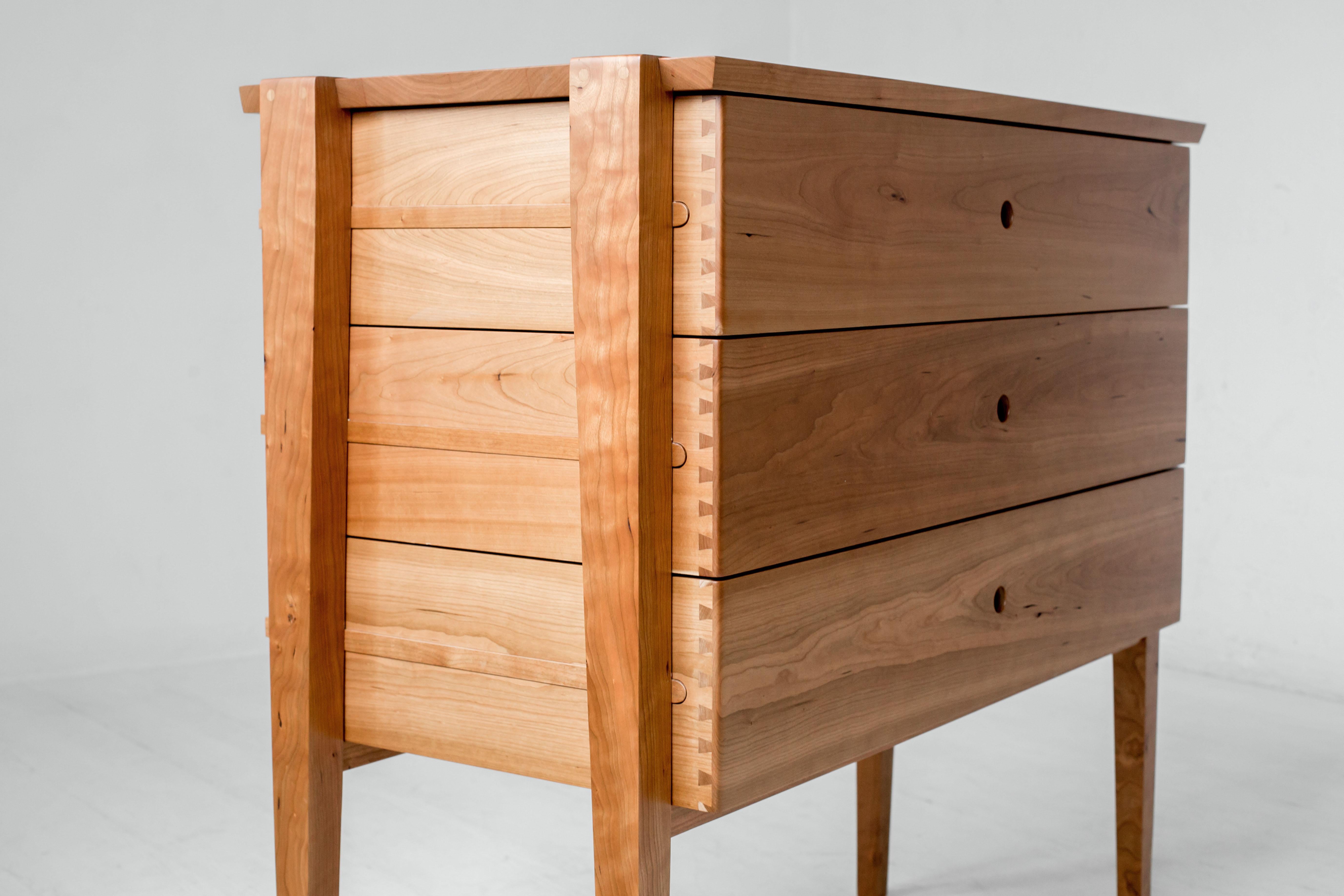 Simplicity and beauty intersect in this modern interpretation of a tradition design. Our Oslo cherry dresser features three deep dovetailed drawers nestled in an open frame. The drawers slide smoothly on waxed wood rails, revealing the mechanism at