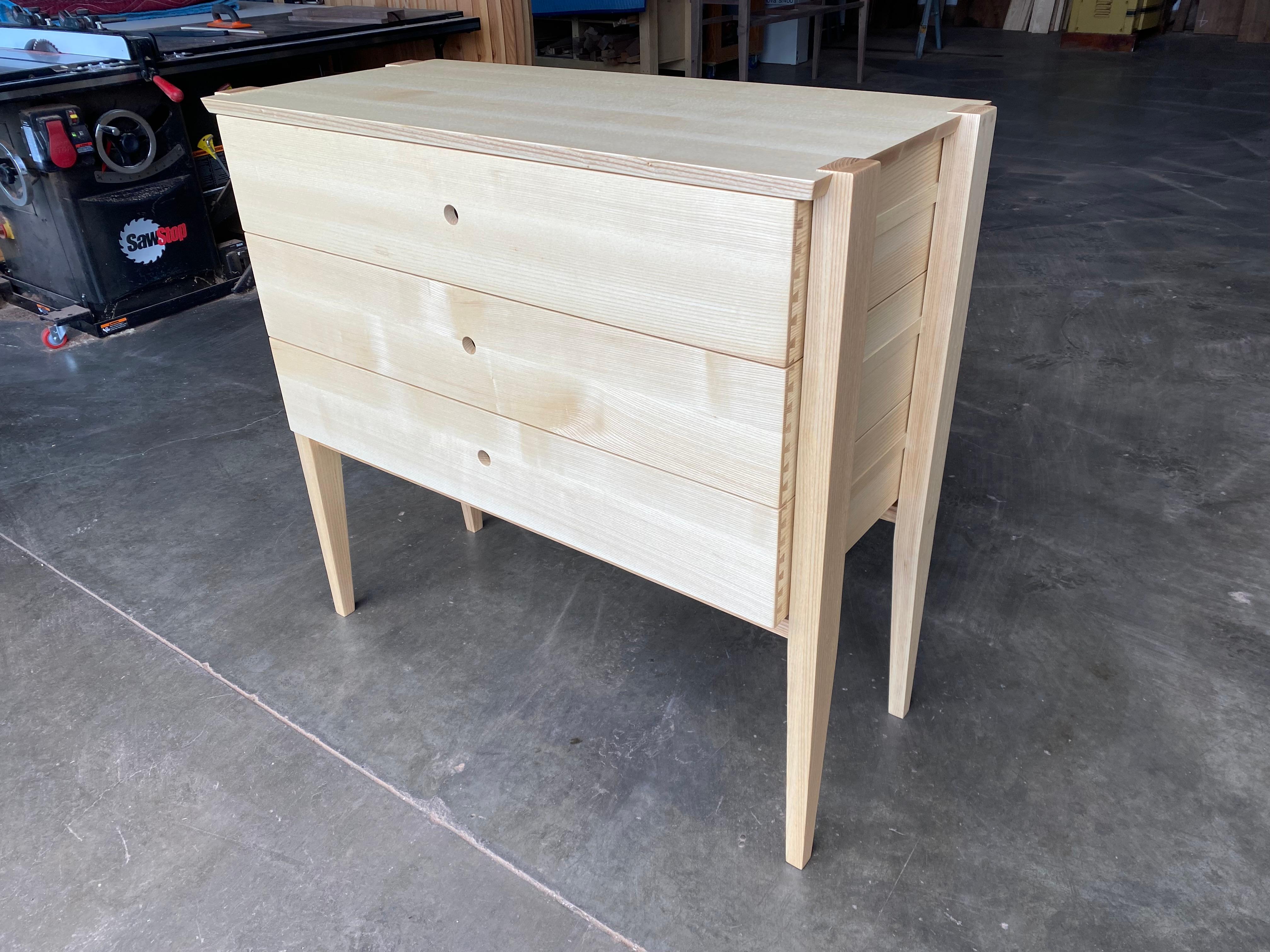 Semplicità e bellezza si intersecano in questa moderna interpretazione di un design tradizionale. Il nostro comò Oslo in frassino segato di quarto presenta tre profondi cassetti a coda di rondine incastonati in una struttura aperta. I cassetti
