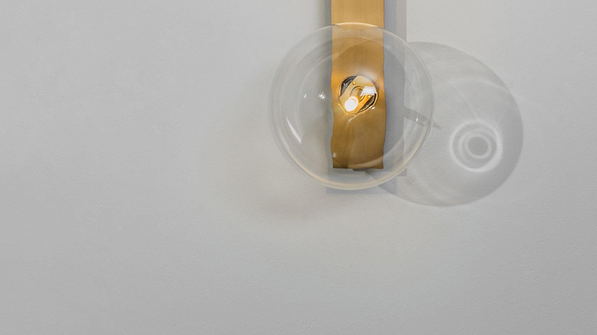 Glass bubbles alight upon a slender rectangle of brass for an essential design. Inspired by the sober compositions of mid-20th century Norwegian artist Ragnhild Keyser, the unique surface curvature of the mouth-blown globes lends a subtle optical