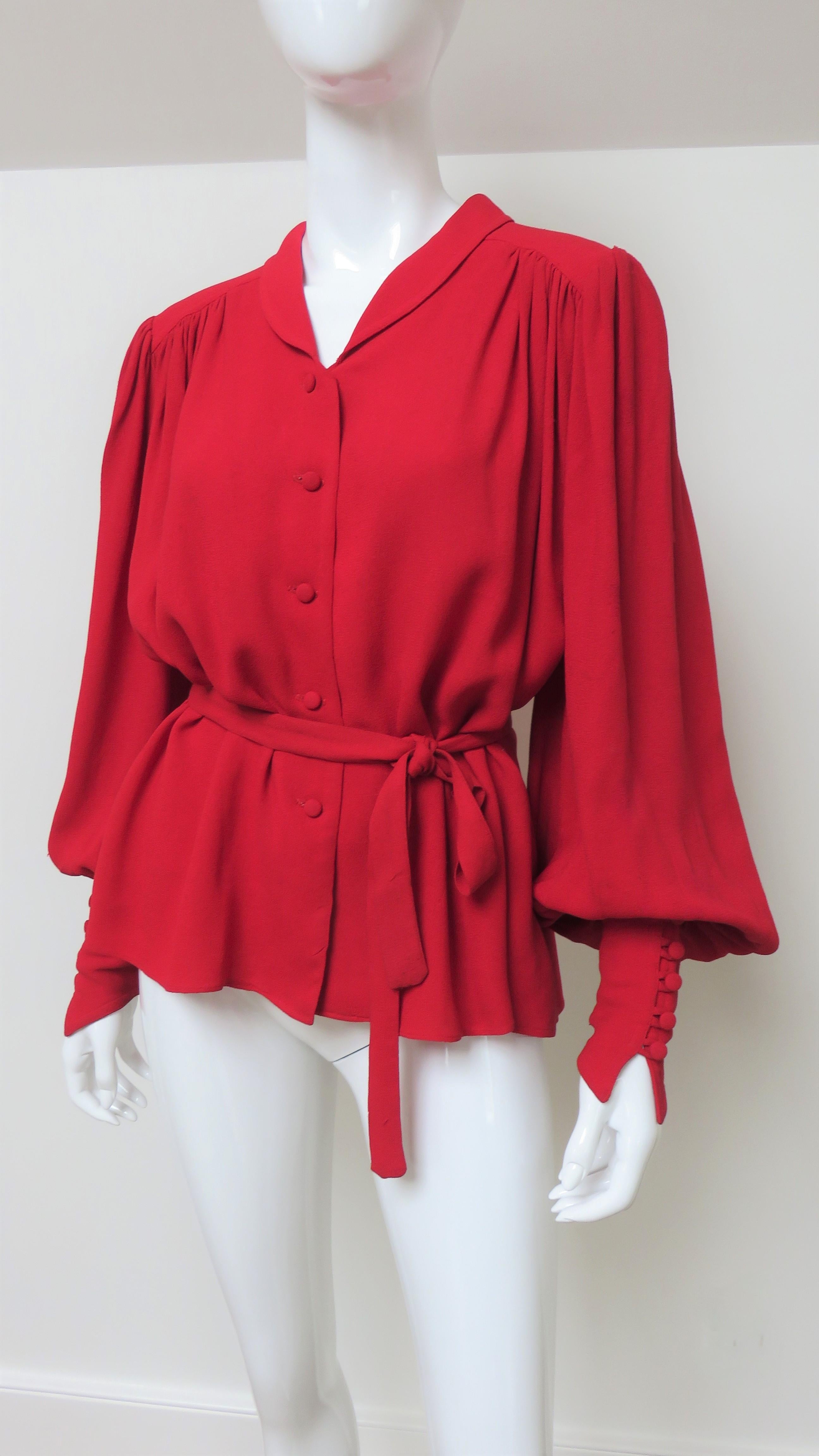 A fabulous red crepe blouse shirt from Quorum designers Ossie Clark and Alice Pollack.  It has a small rounded shirt collar, back yoke and full sleeves with wide pointed cuffs and self covered buttons and loops cuffs. The shirt body and sleeves