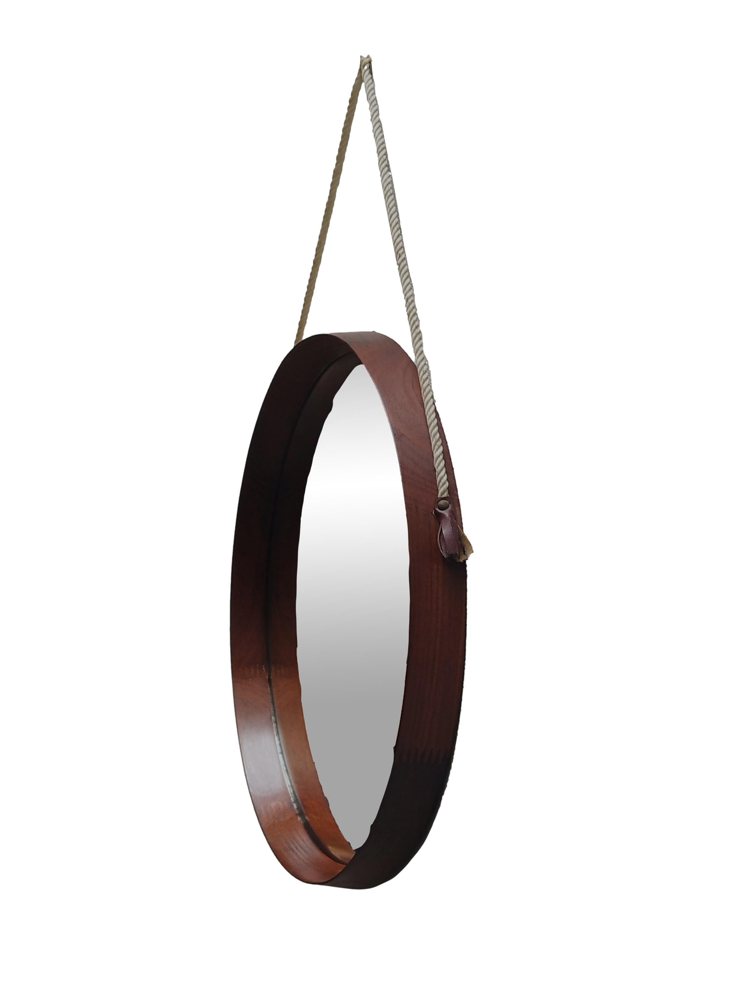 A circular wall mirror of Swedish manufacture, designed by Uno & Osten Kristiansson and produced by Luxus in the 1960s, it features a curved teak wood frame including a cord and leather strap for attachment.