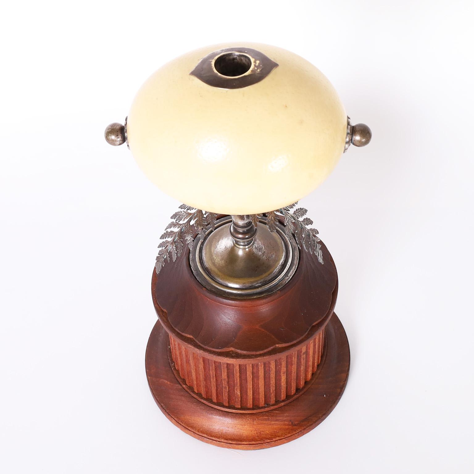 Lofty mid century candlestick with a found object composition having an ostrich egg candle cup over three metal leaves and a pedestal in a classical wood carved base.