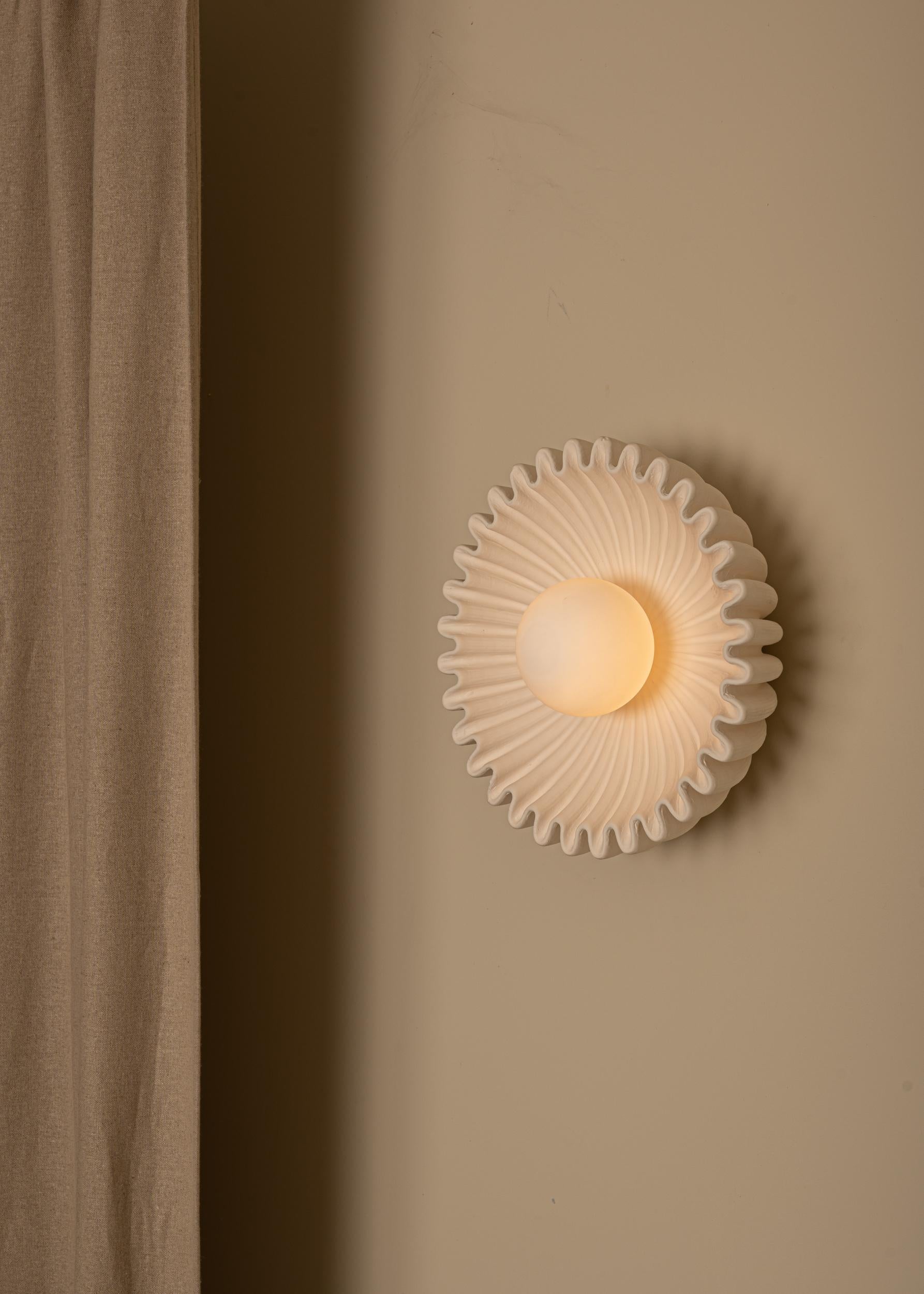 An outstanding piece made of a detailed ceramic shell, nesting a glass globe at its center, difusing a soft milky light. Both functional and sculptural, the Ostro wall light is unique and it is as beautiful alone or in pairs.