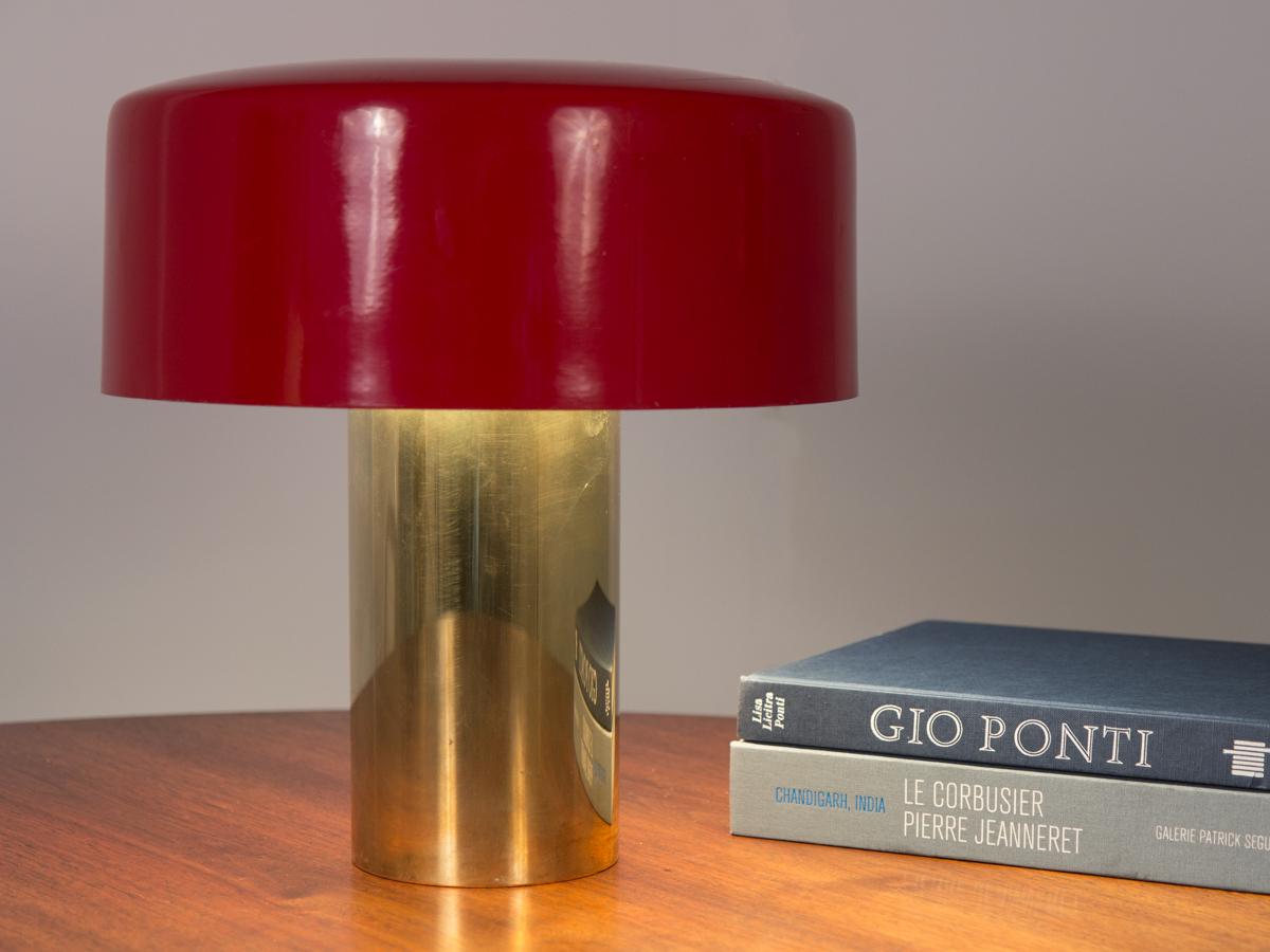 Statement table lamp, attributed to Giuseppe Ostuni and manufactured by his lighting company Oluce. Simple yet striking. The bold-red enameled metal shade rests on three brass prongs on cylindrical reflective brass base. In fine working order with