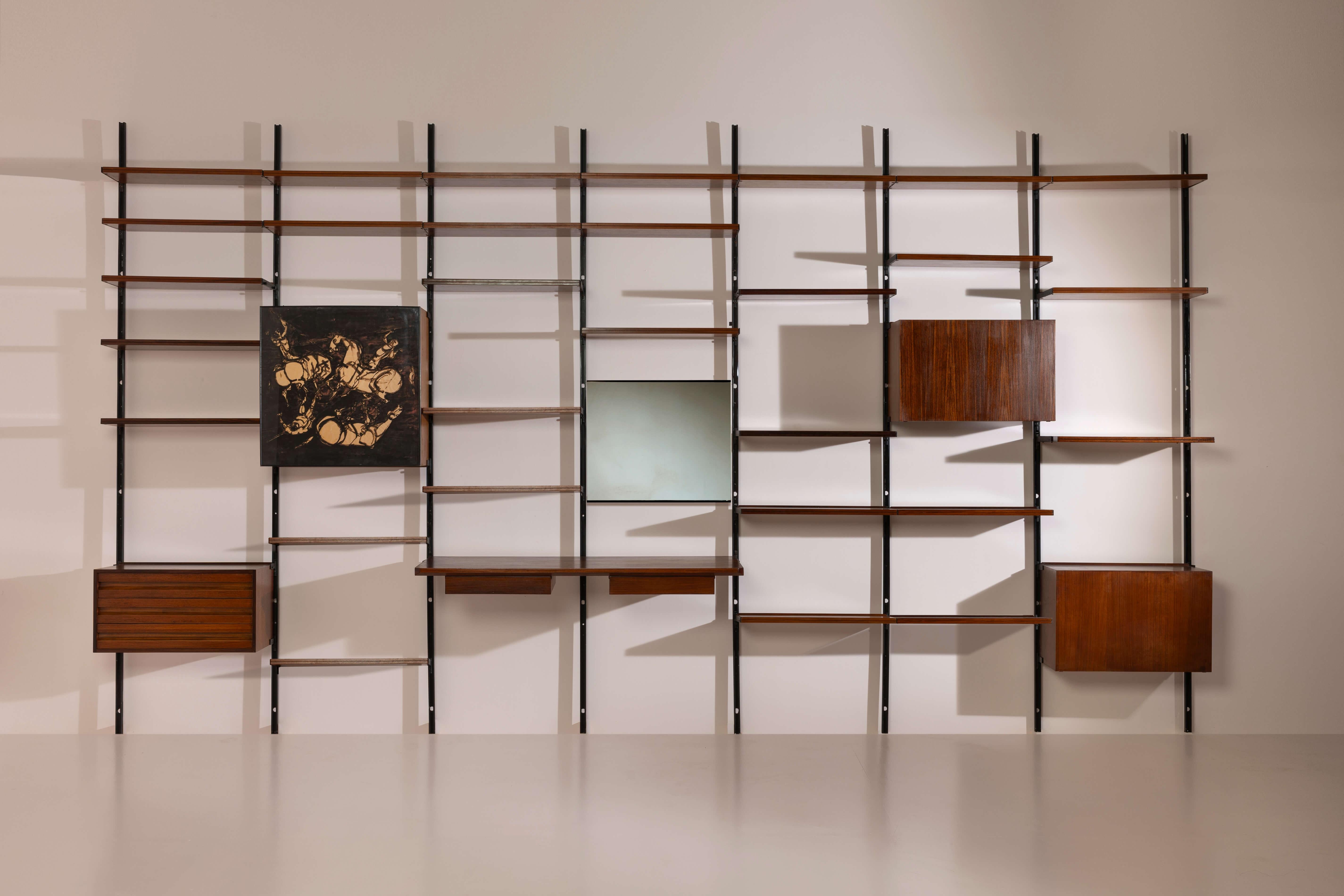 This E22 modular bookcase/wall system, conceived by Osvaldo Borsani for Tecno, presents a remarkably poetic and functional architecture of display and storage. The composition begins with a grid of tall, slender vertical uprights in black metal,