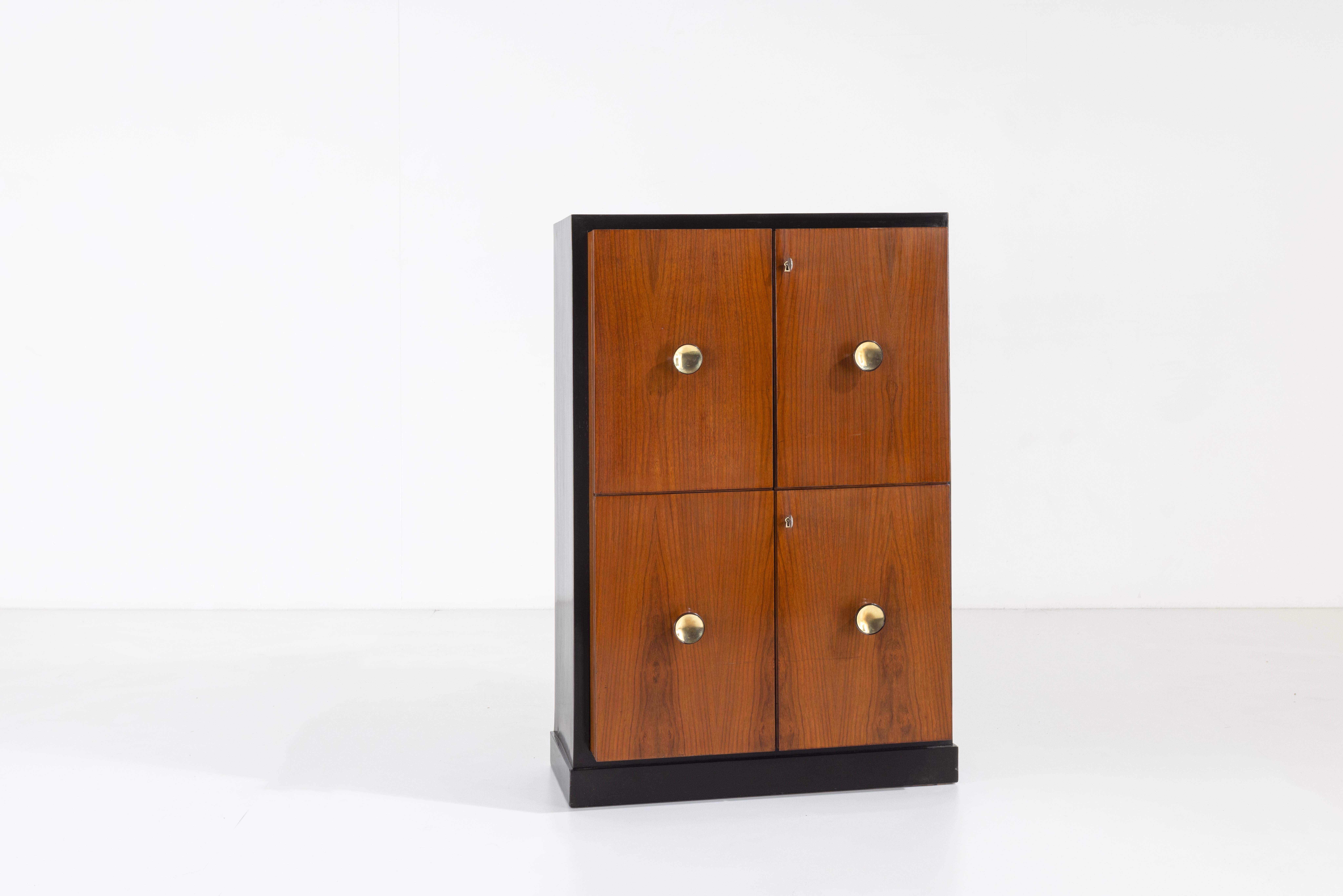 This unique piece of furniture is an elegant storage unit that fits perfectly in both the living room and bedroom. The main structure in ebonized wood contrasts with the natural wood of the doors, which are enhanced by turned brass handles to act as