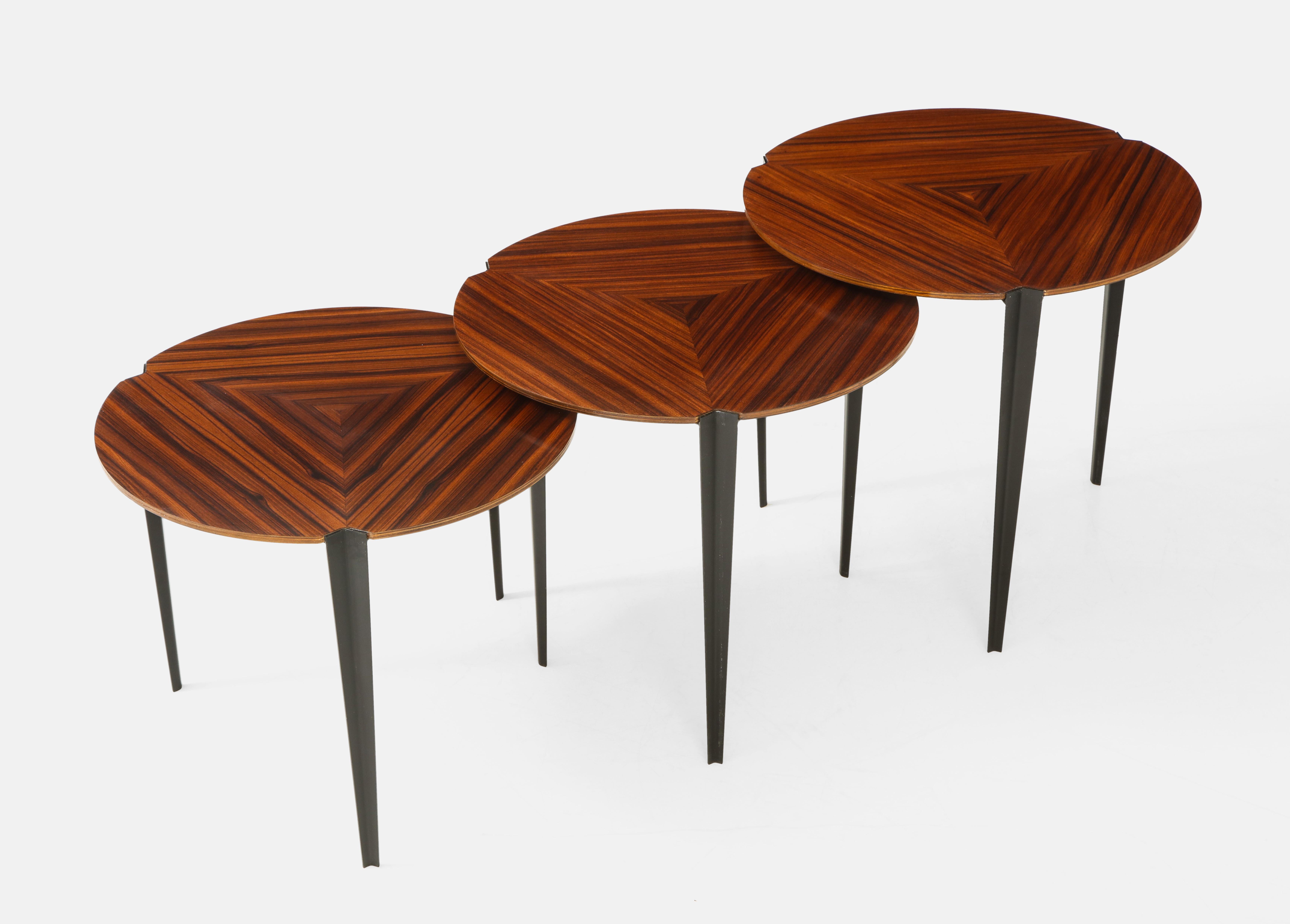 Osvaldo Borsani for Tecno set of 3 modernist nesting tables with rosewood veneer tops on three black enamel tapering metal legs, Italy, circa 1957. The table tops consist of three stark grained wood veneer pieces assembled to create a graphic