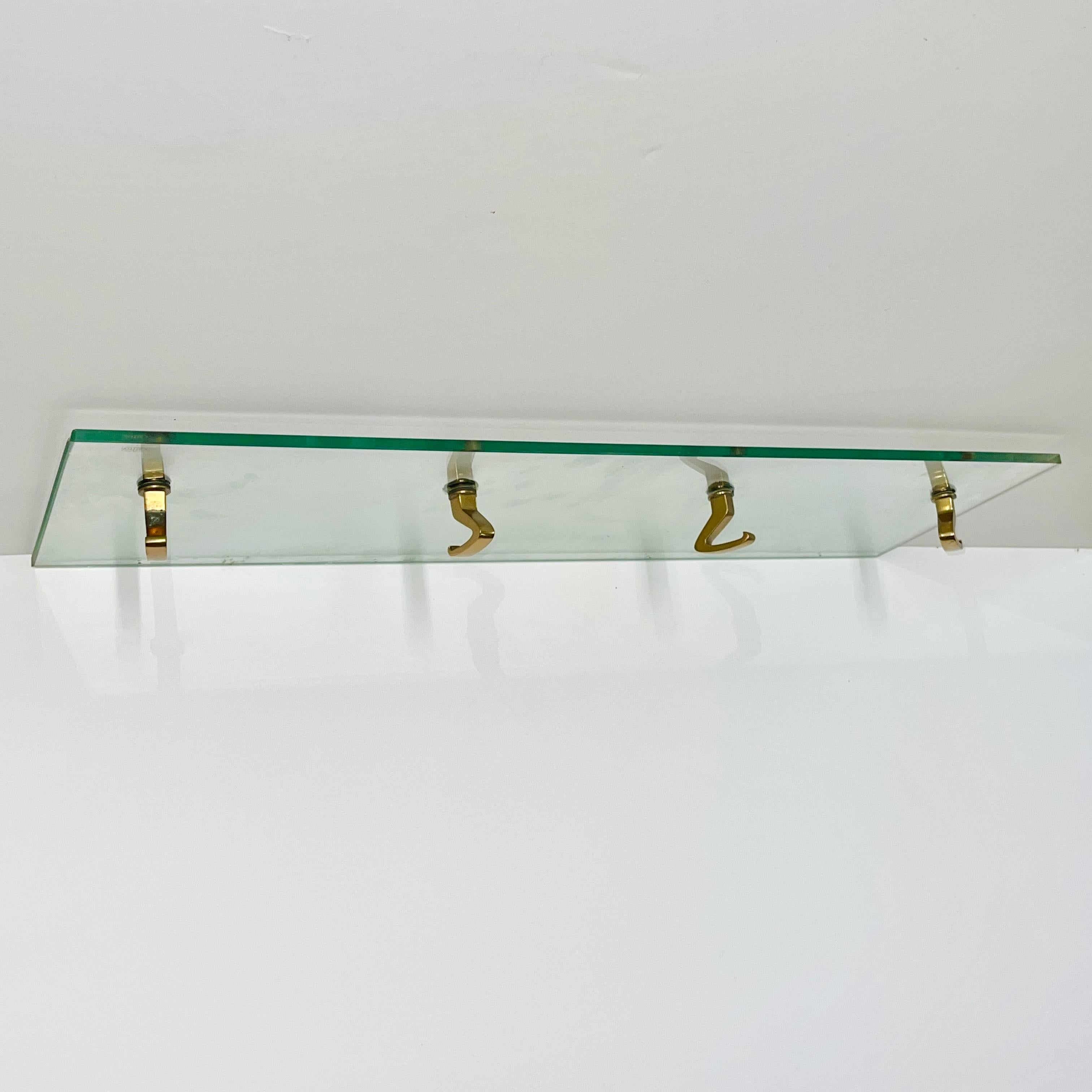 Original 1940's brass swiveling coat hooks mounted to a Vitrex tempered glass shelf designed by Osvaldo Borsani, Italy.
See catalog image from the Borsani Archives.
This shelf is meant to be mounted perpendicular to a wall with commercially