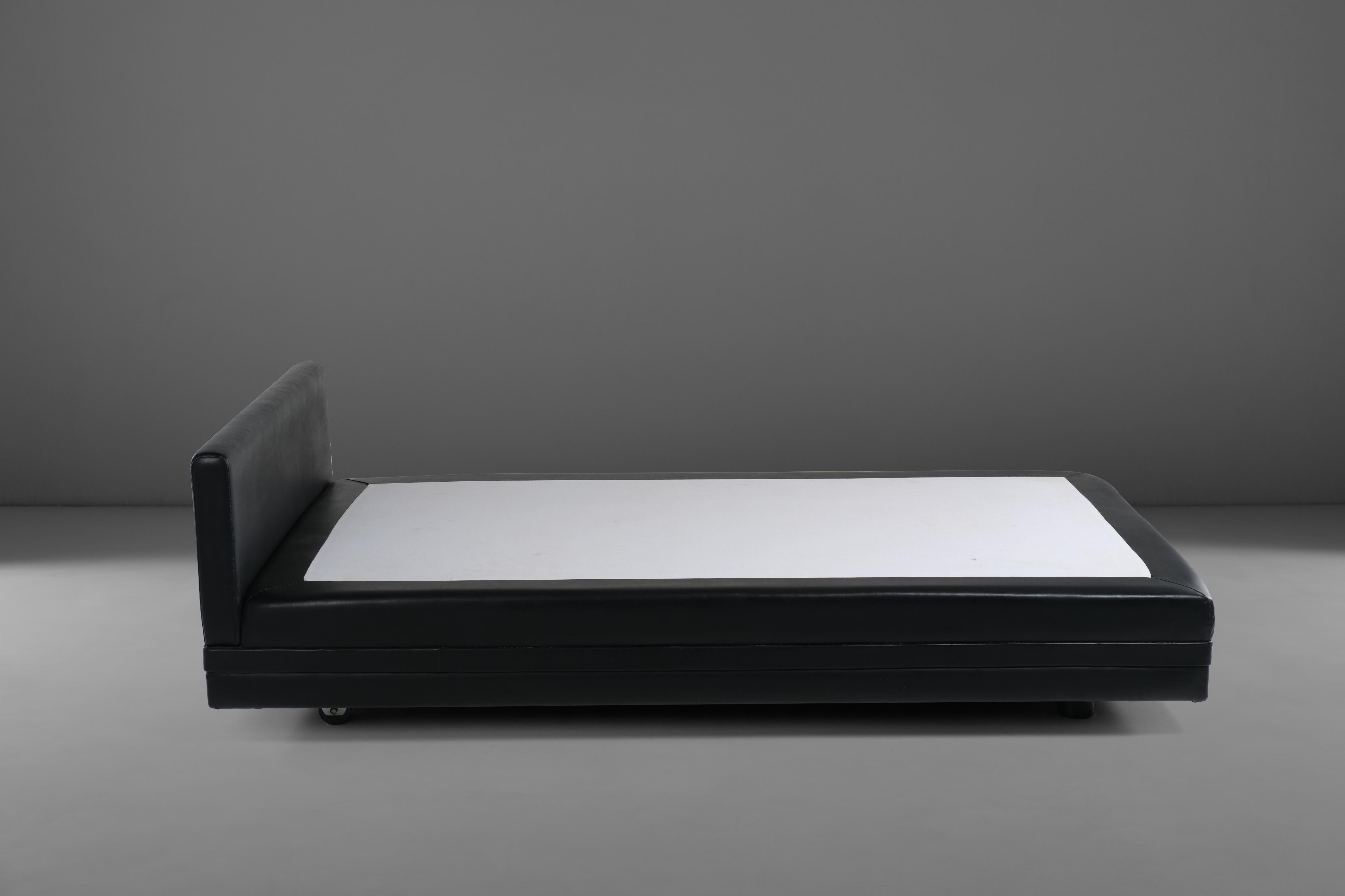 Das 1967 von Osvaldo Borsani für Tecno entworfene Bett ist mit seiner Metallstruktur, dem Pad aus Polyurethanschaum und dem Bezug aus schwarzem Kunstleder ein echtes Beispiel für postmodernes Design. Der gesamte Bettrahmen wird durch einen Gurt aus
