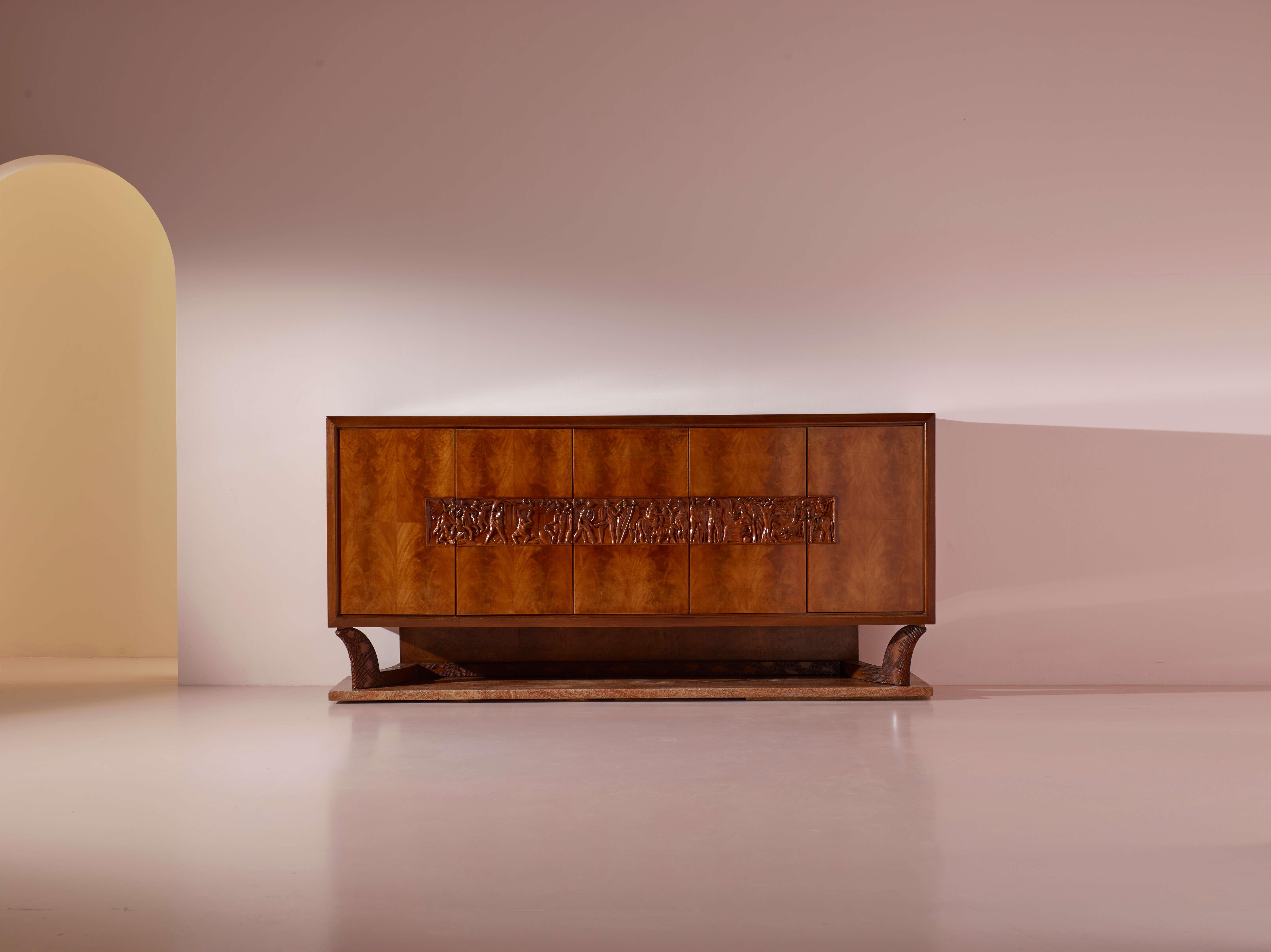Grande credenza con ante impiallacciate in noce e cassetti interni, caratterizzata da un inserto in bassorilievo in legno massiccio intagliato raffigurante figure mitologiche e da una base in marmo Rosso Fiorentino. Attribuita a Osvaldo Borsani e