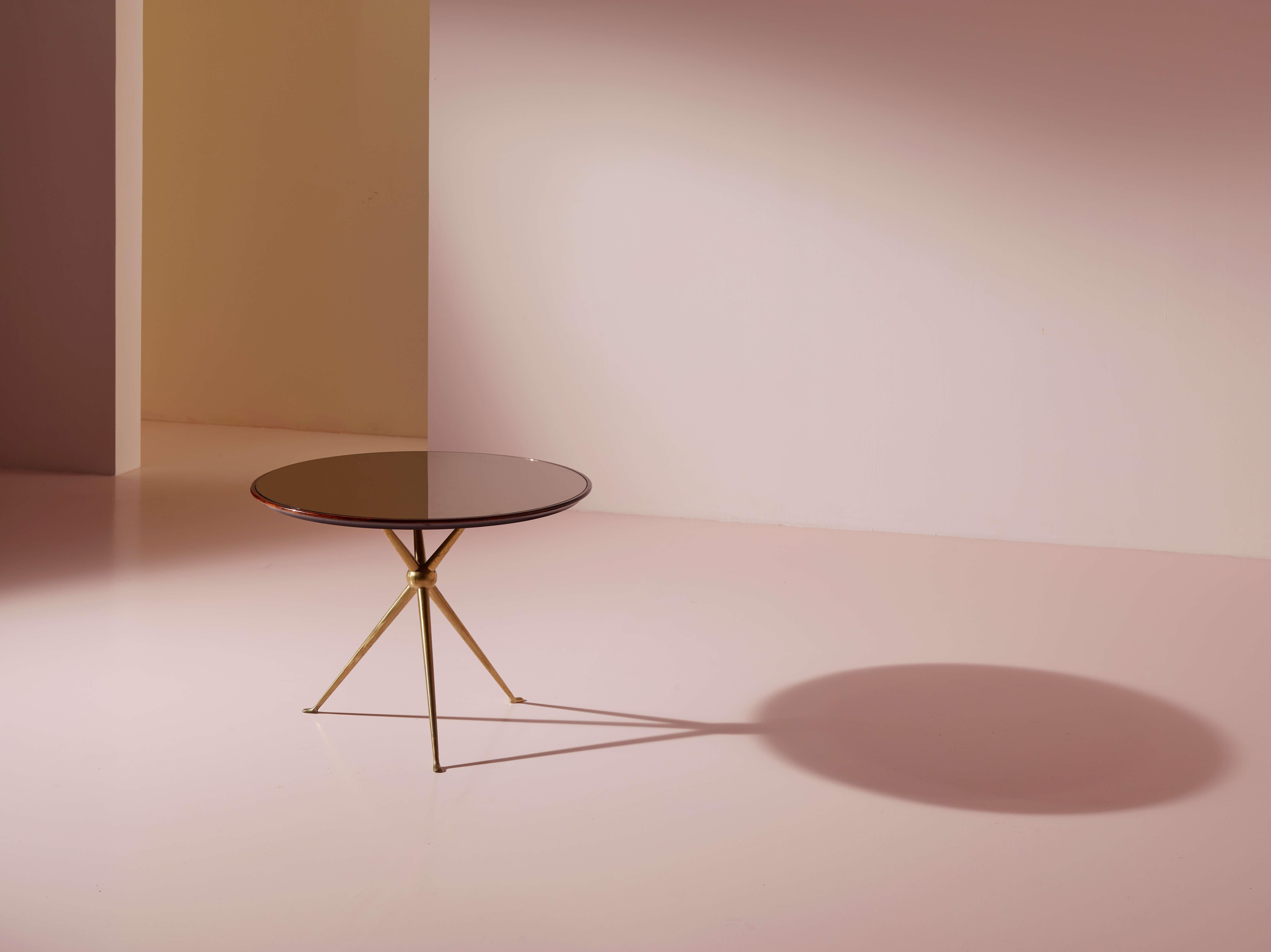 Tavolino rotondo in noce con piano in vetro a specchio e base a treppiede in ottone, manifattura Arredamenti Borsani Varedo, anni '50, design di Osvaldo Borsani.

Una superficie circolare in noce africano e vetro specchiato emerge come elemento