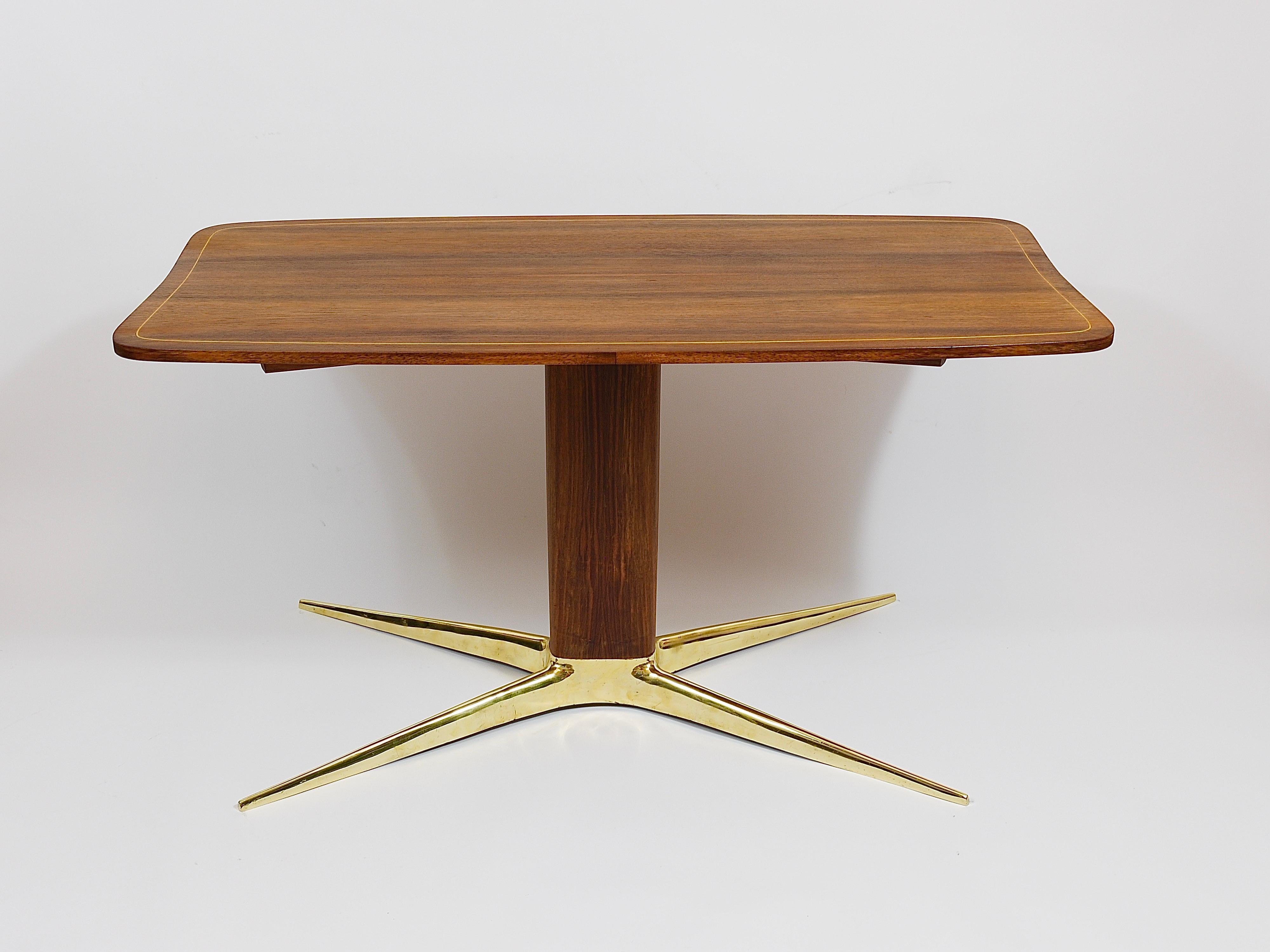 Une élégante table basse ou table de canapé des années 1950, conçue par l'architecte et designer autrichien Oswald Haerdtl. Une belle table avec un beau plateau incurvé, une tige centrale ovale en noyer et la base typique en forme de X, en laiton