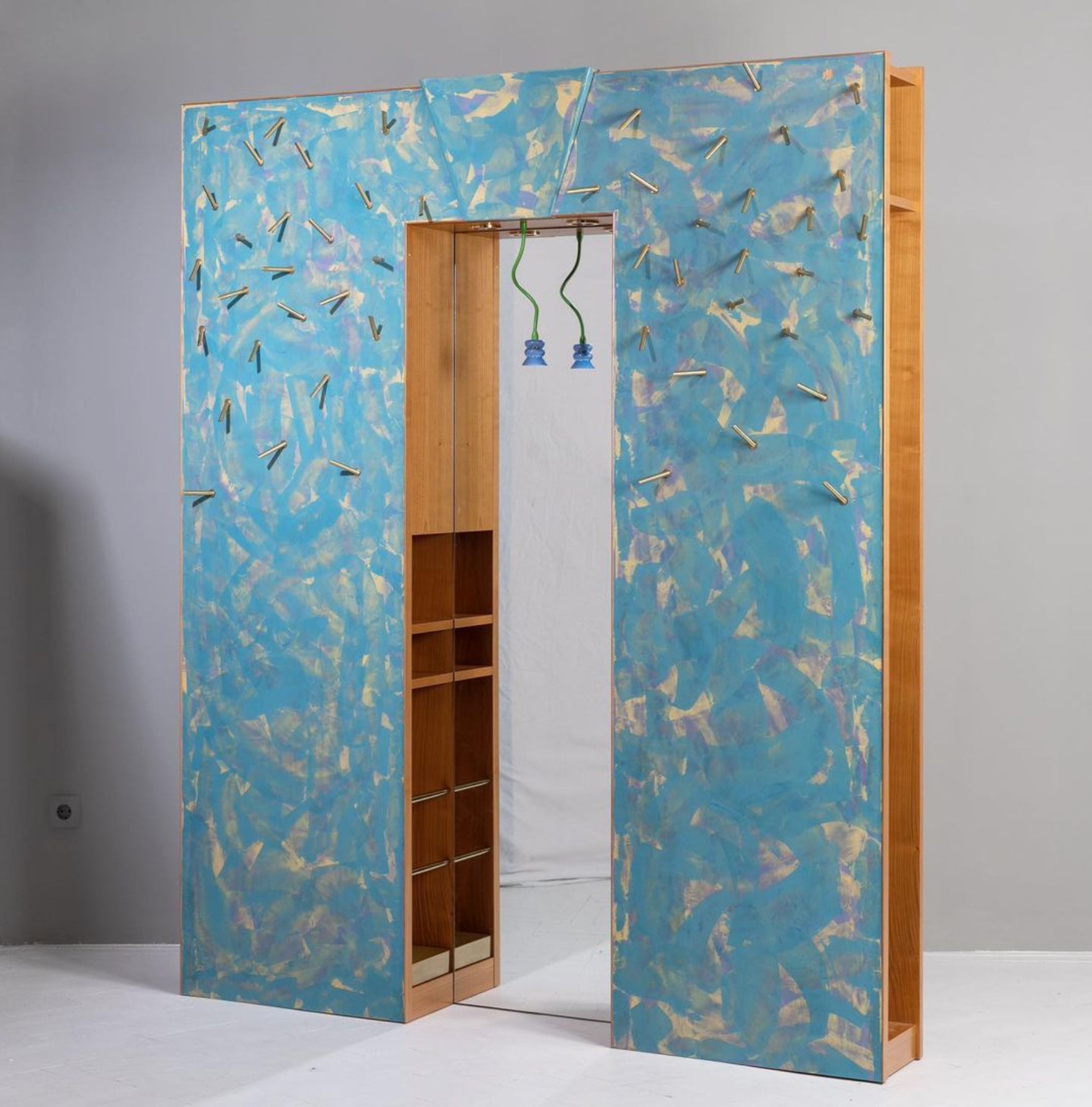 The “OTKA” wardrobe unit was designed by Borek Sipek for “Pietat/ Imitat/ Ritual” series produced by Leitner Interior Design in the 1990s. The unit is made of hand-painted wood and features brass elements and a glass lamp in front of the mirror.