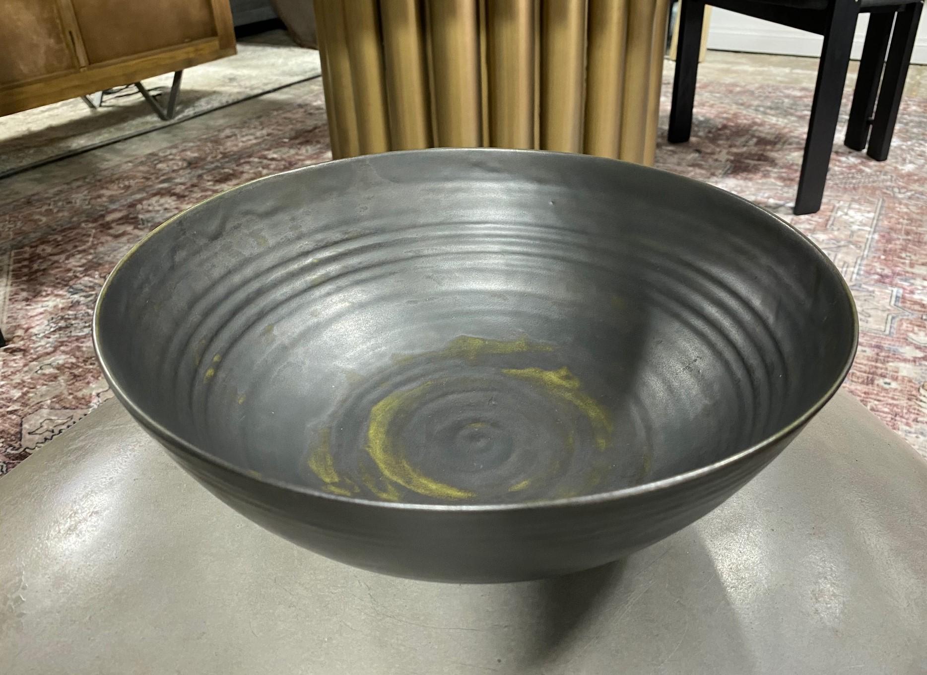 A masterful work by famed potters Otto and Gertrud Natzler. This monumentally large round-shaped footed bowl was wheel thrown and formed by Gertrud and glazed by Otto with a rare matte black glaze with hints of avocado green working their way to the