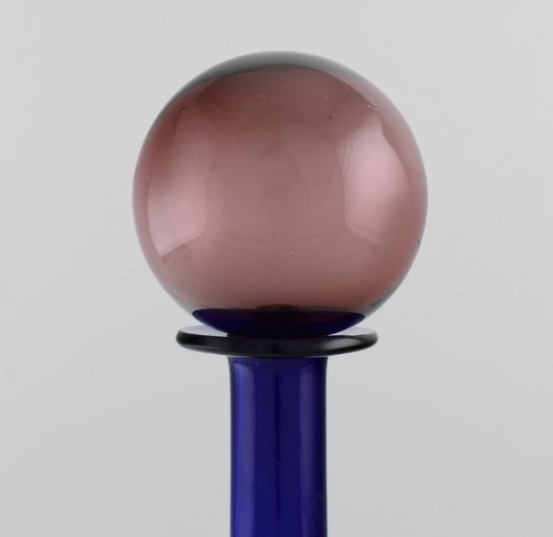 Otto Brauer für Holmegaard. 
Vase / Flasche aus blauem mundgeblasenem Kunstglas mit lila Kugel. 
1960's.
Maße: 34,5 x 9,5 cm (inkl. Kugel).
In perfektem Zustand.