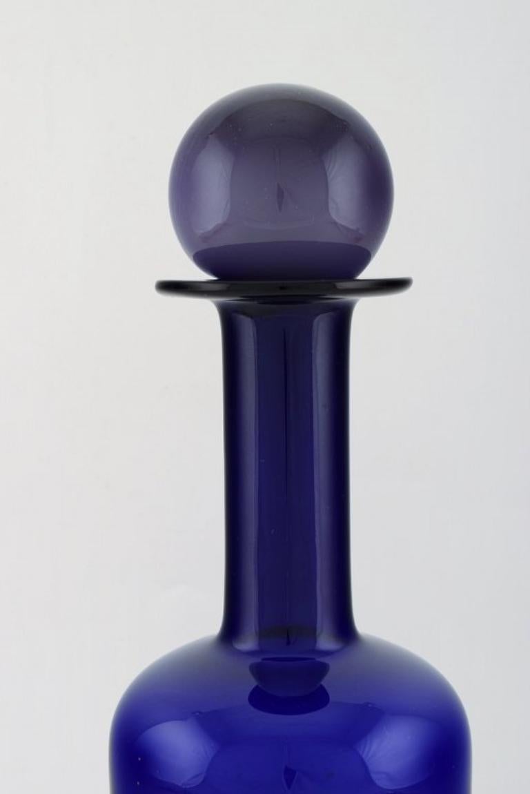 Otto Brauer für Holmegaard. 
Große Vase / Flasche aus blauem Kunstglas mit lila Kugel, 1960er Jahre.
Maße: 36,5 x 12 cm (inkl. Ball).
In perfektem Zustand.