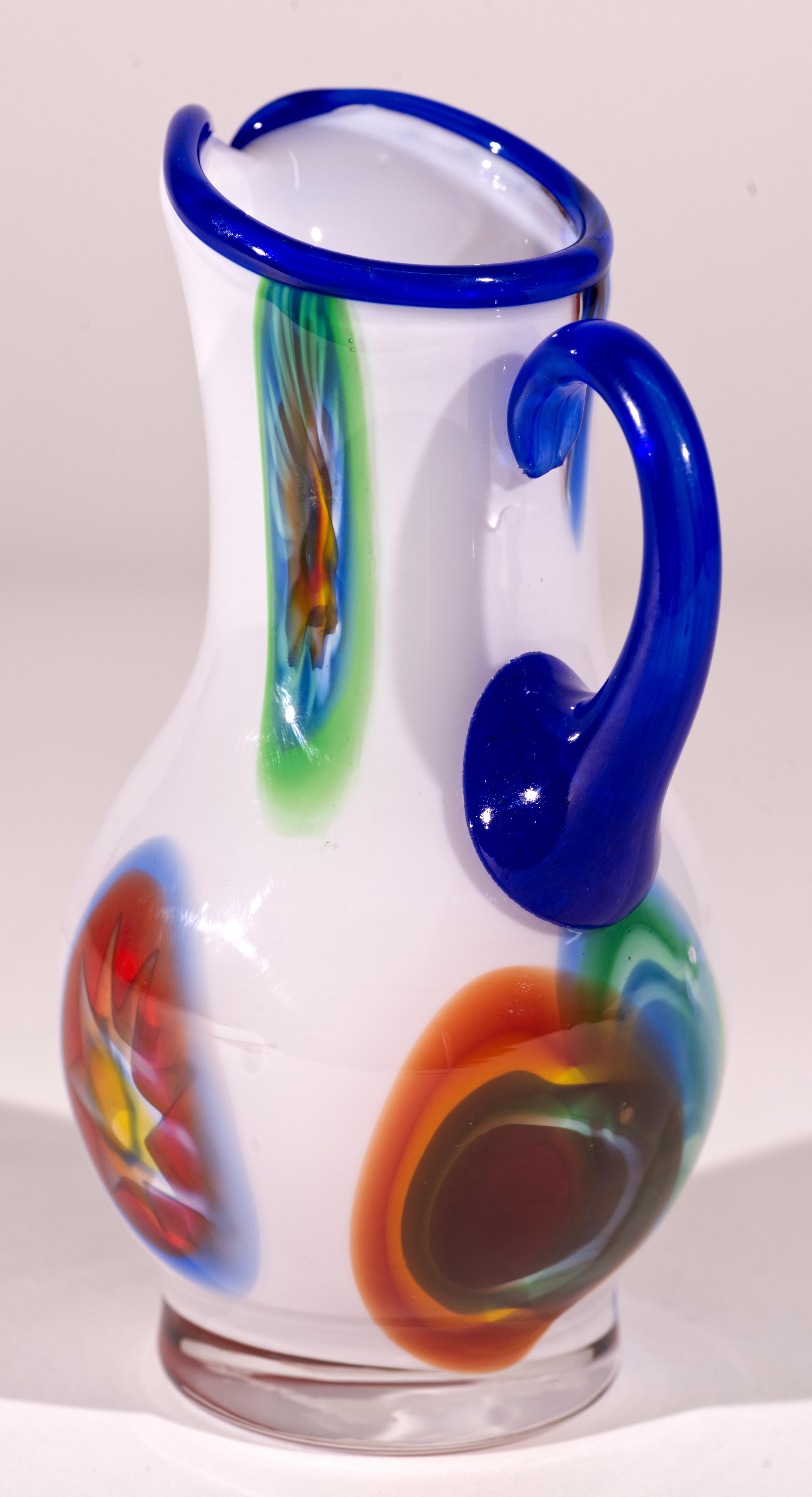  Whiting, vaso a forma di bocciolo in vetro artistico con inclusioni millefiori multicolori, disposte in un motivo astratto su uno sfondo di vetro bianco. Il manico e il bordo in vetro blu semi-opaco accentuano i colori vivaci del disegno. Il vetro