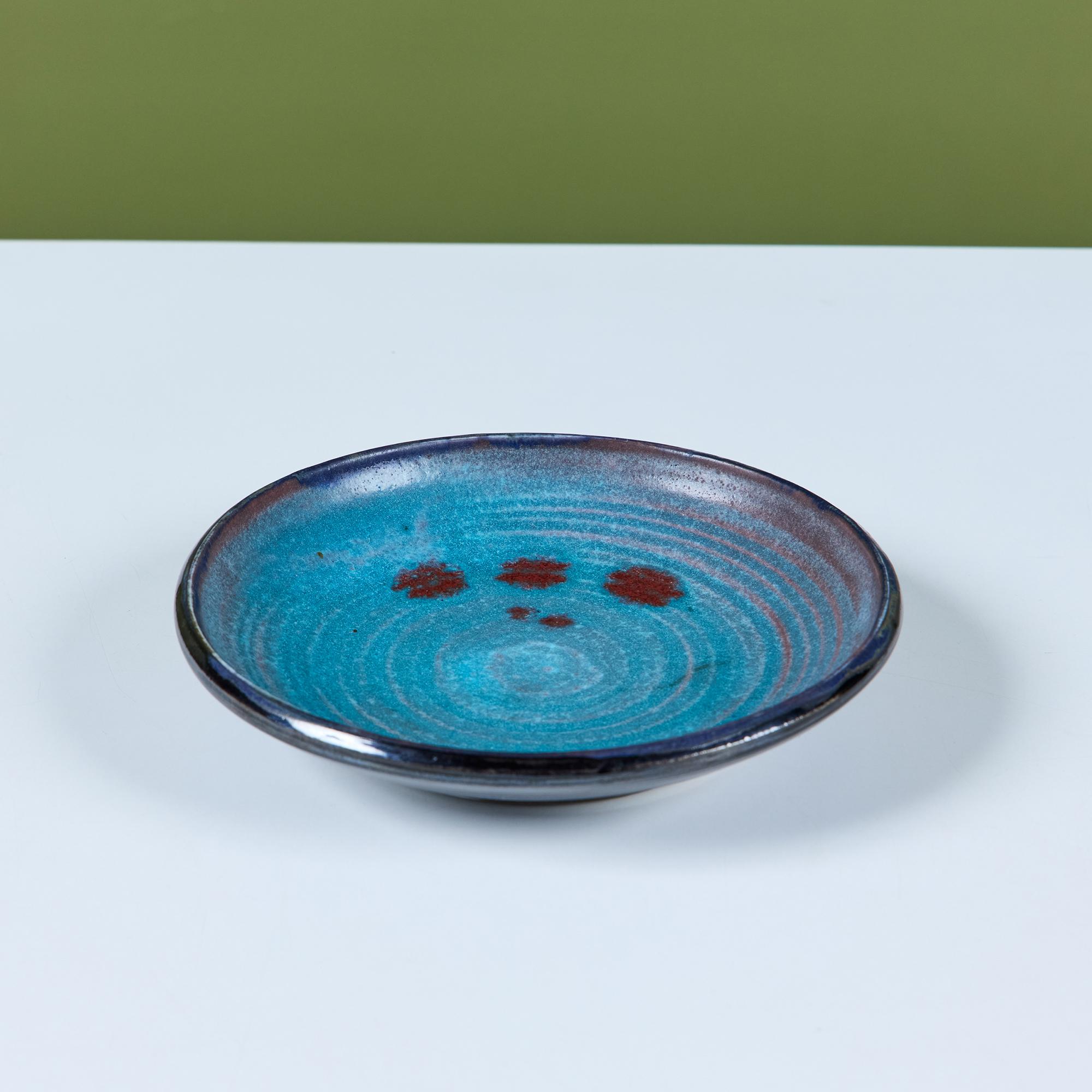 Un piccolo piatto in studio Pottery dell'importante ceramista del 20th Century Studios Otto Heino. Questo esemplare presenta le nervature delle dita con una smaltatura blu e rossa, che in alcune aree si fonde con una foschia violacea. Il piatto