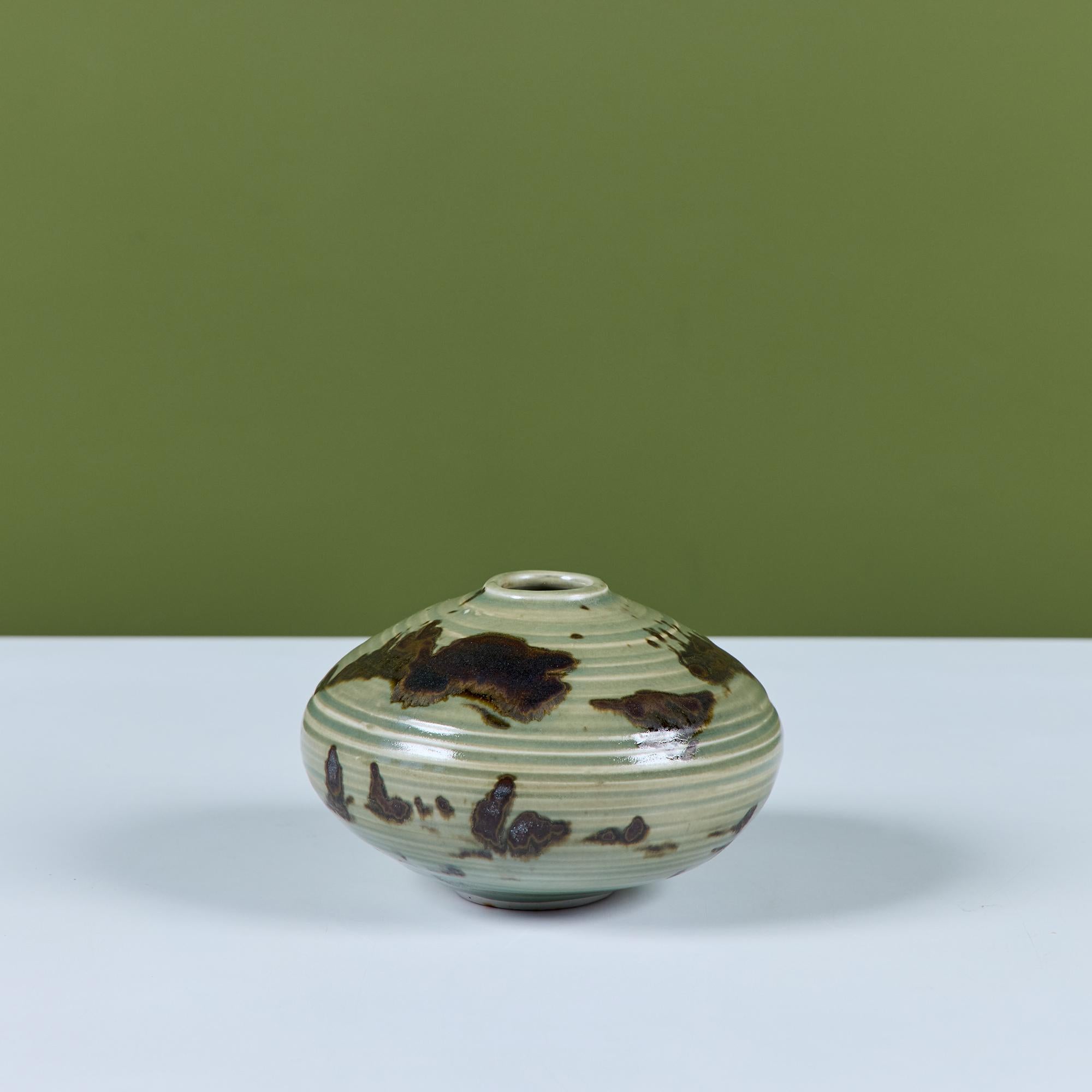 Un piccolo vaso in studio Pottery dell'importante ceramista del 20th Century Studios Otto Heino. Questo vaso a bocciolo arrotondato è caratterizzato da uno smalto verde all over e da una struttura a coste con spruzzi di marrone.  Firmato sul lato