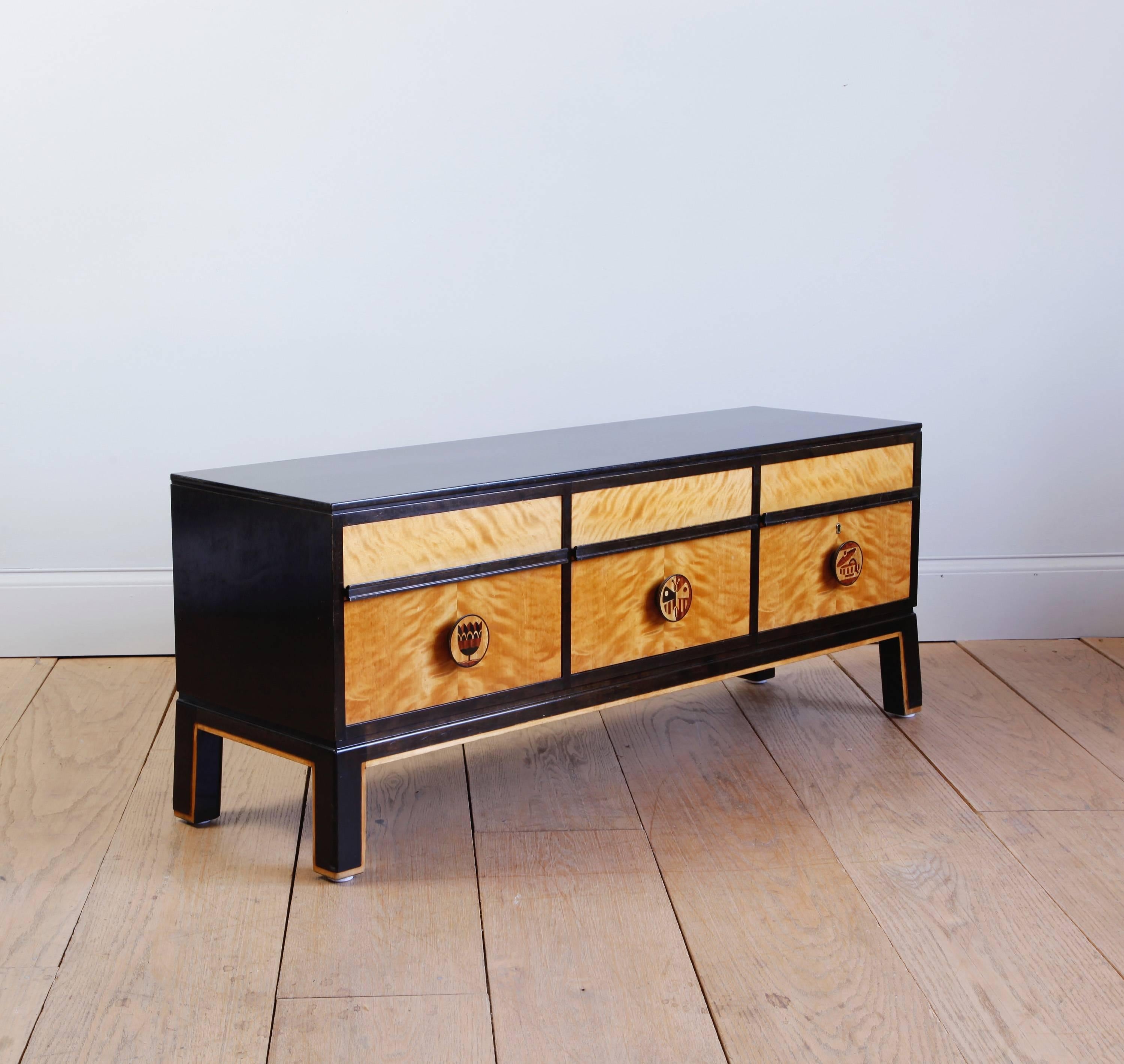 A low, six-drawer chest made of flame birch and black lacquered wood. The knobs are inlaid with various contrasting woods to create playfully elegant figures which were one of the distinctions of Schulz's creations for Boet. 

Otto Schulz was an