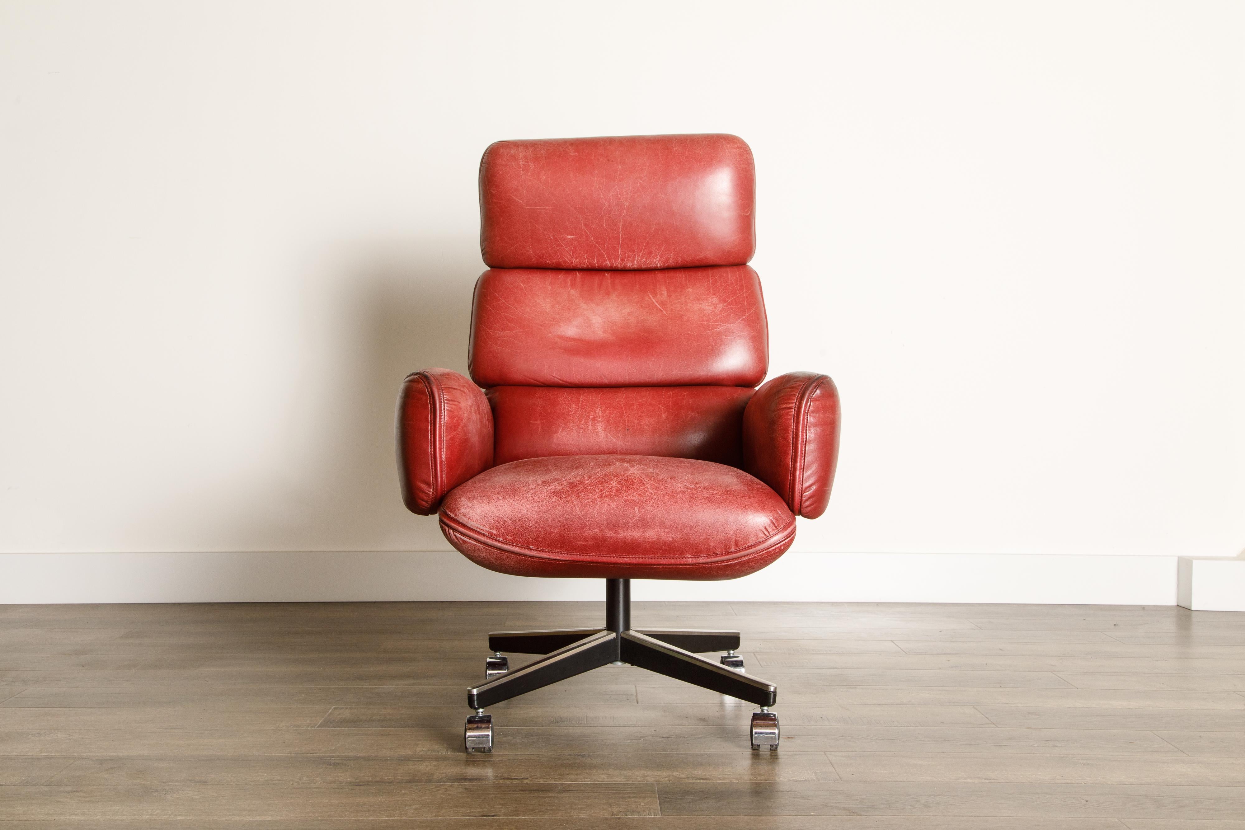 This gorgeous highly patinated burgundy leather highback executive desk chair is by Otto Zapf for Knoll International, circa 1981 . Constructed of heavily cushioned sections, with the top head section and arms removable. The chair base is height and