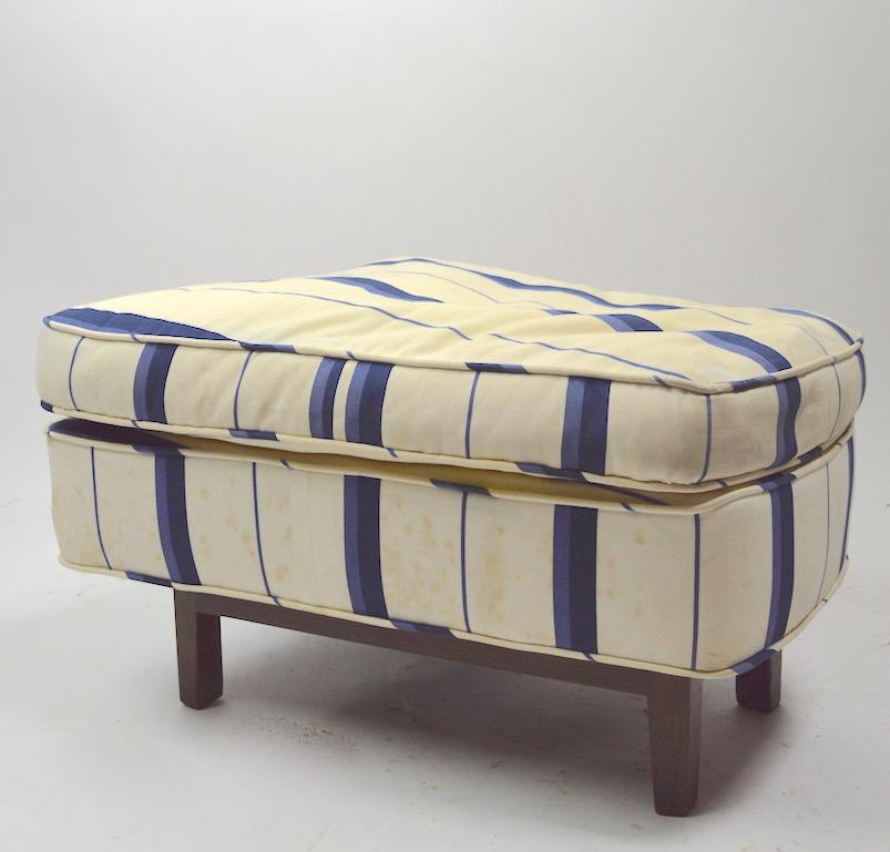 Ottoman, footrest manufactured by Dunbar. This example is structurally sound, and sturdy, it shows cosmetic wear and will need to be reupholstered. Asymmetrical form, upholstered top on solid wood base.