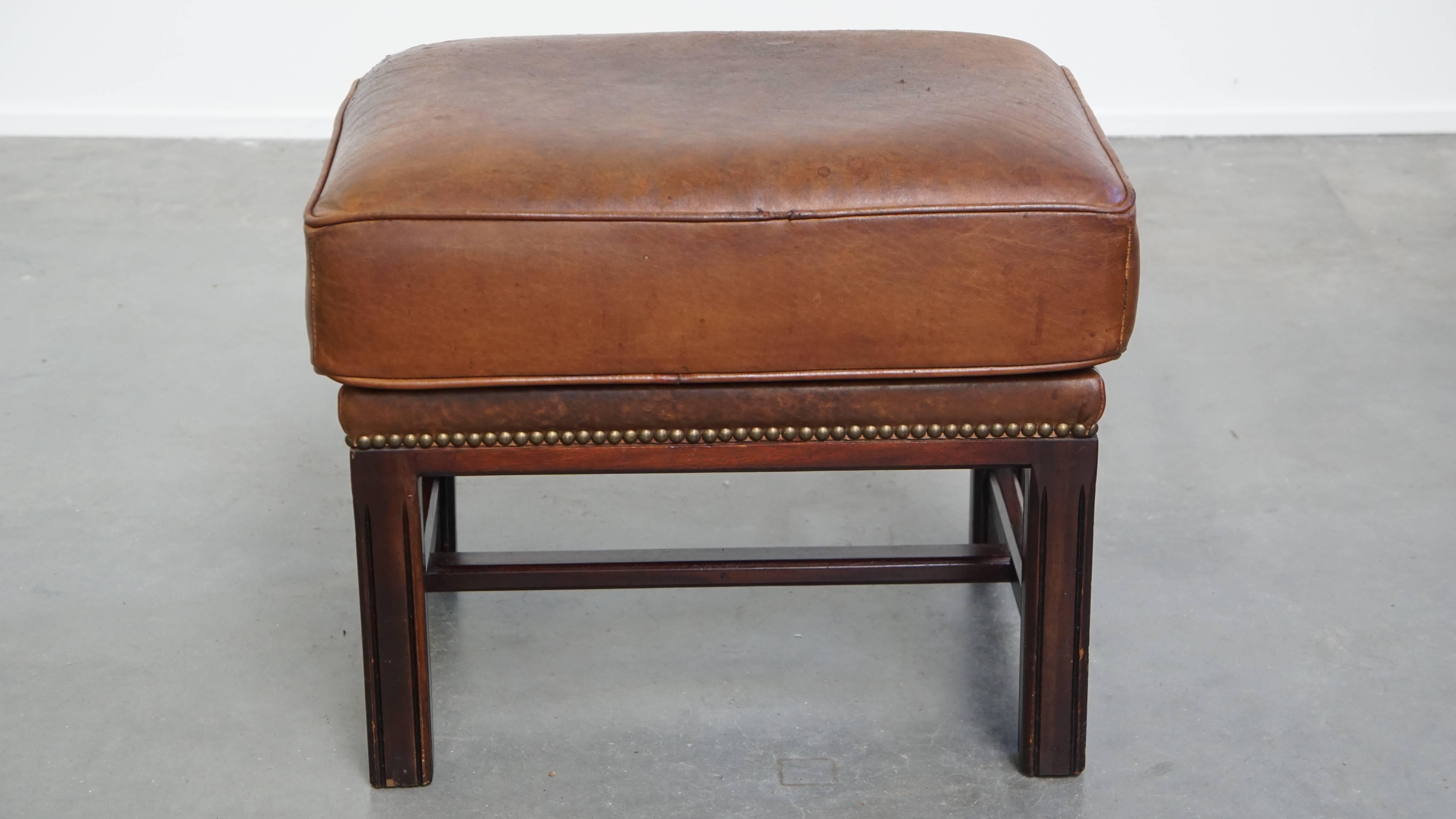 Offered here is this ottoman made of sheepskin leather with a wooden frame and finished with decorative nail trim. A sheepskin leather footstool, also known as an ottoman, transforms your already comfortable armchair into a true relaxation paradise.
