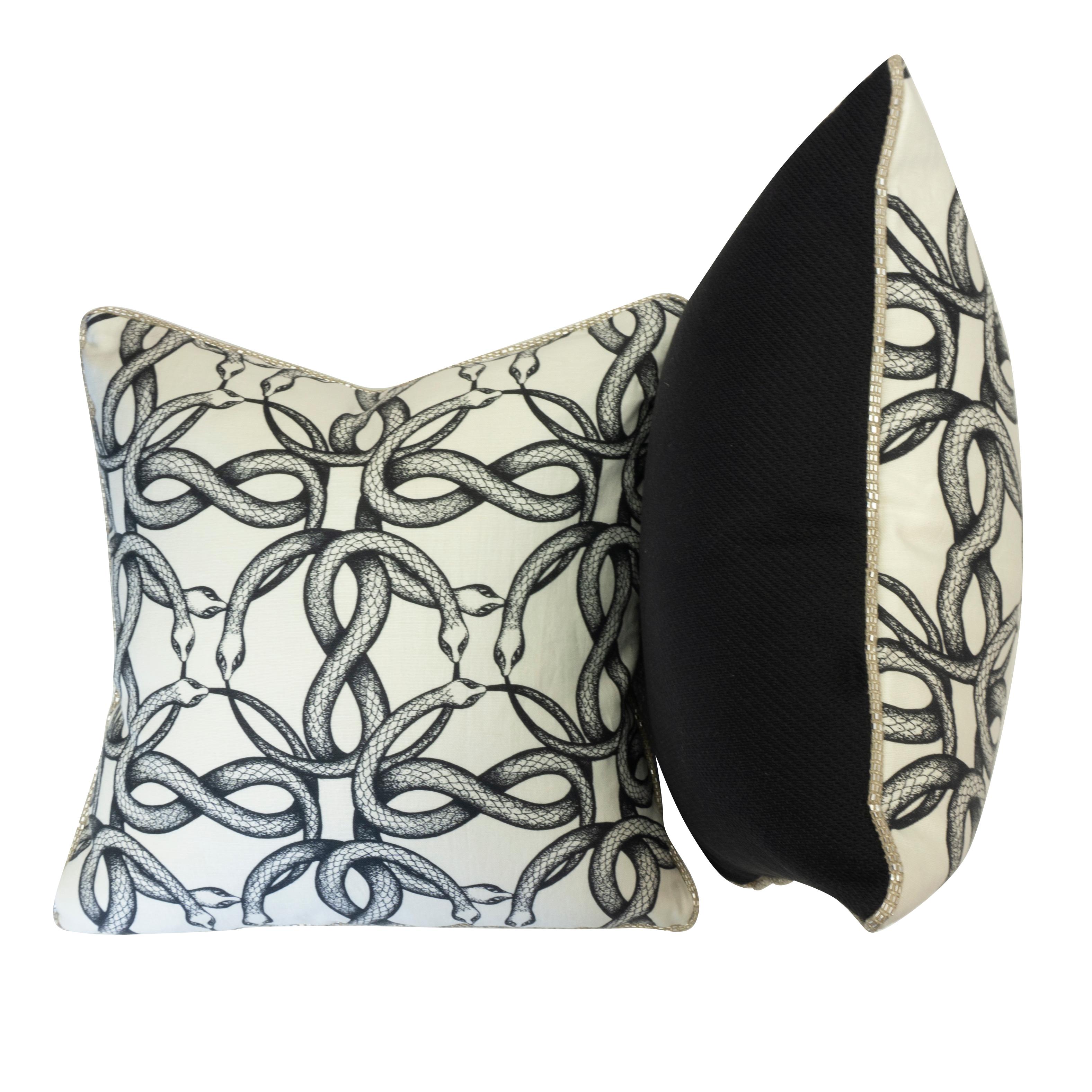 A pair of square throw pillows made with Pierre Frey’s Ouroboros fabric which depicts a printed snake pattern; inspired by the Greek eternal cycle symbol. Completed with a solid black cotton backing and a special woven metallic piping for the